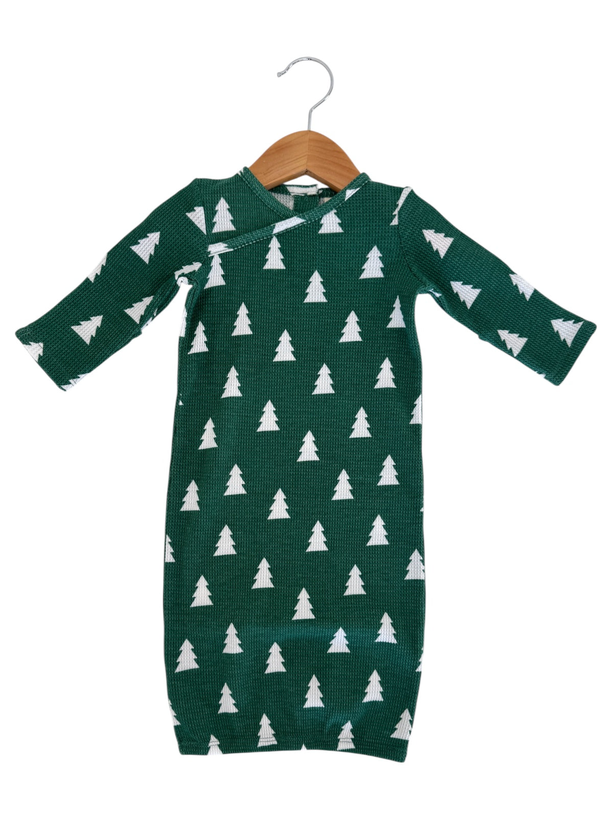 Green baby outfit with white tree patterns, hanging on a wooden hanger.