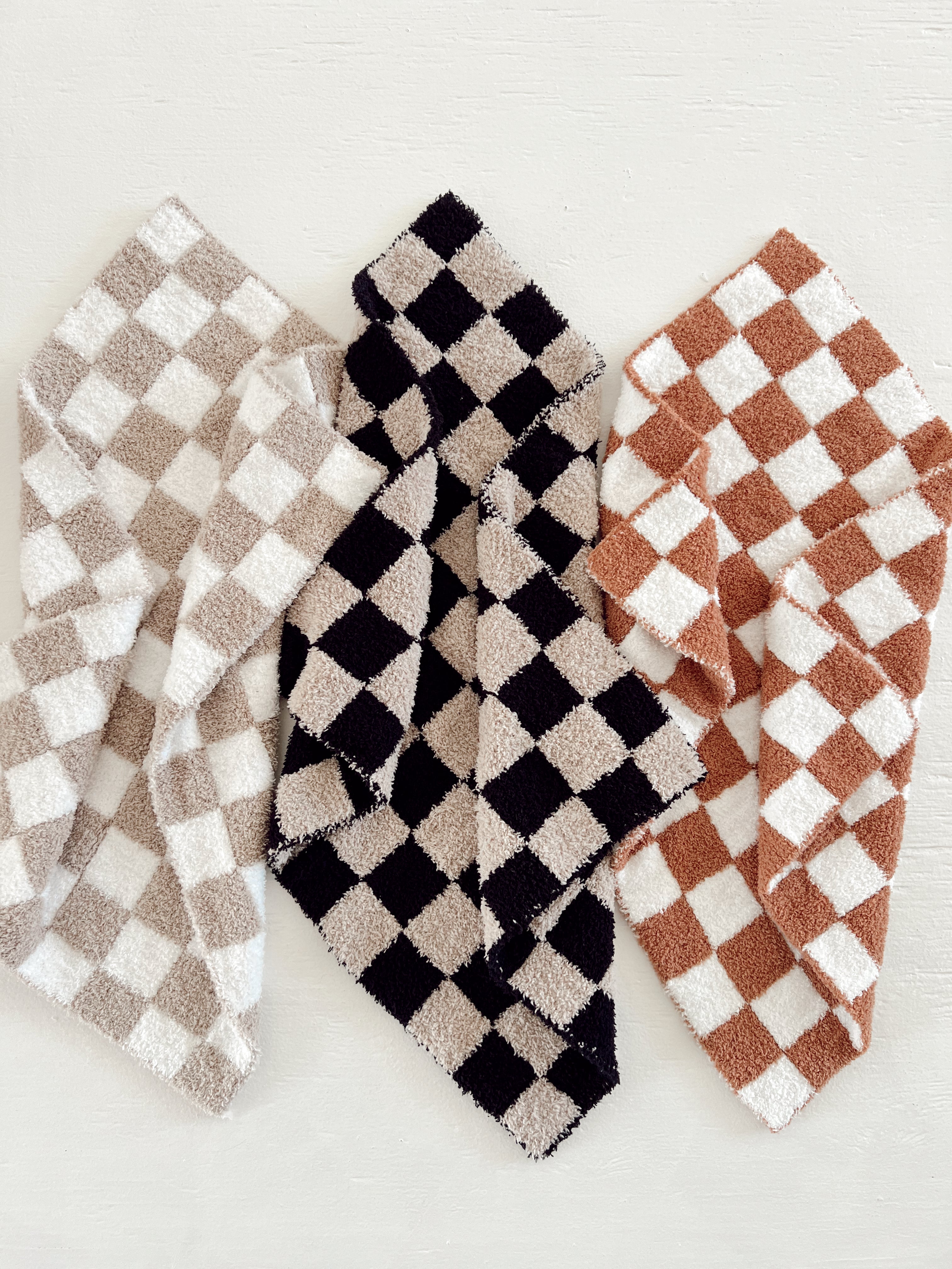 Three checkered towels in beige, black, and rust colors arranged on a light surface.