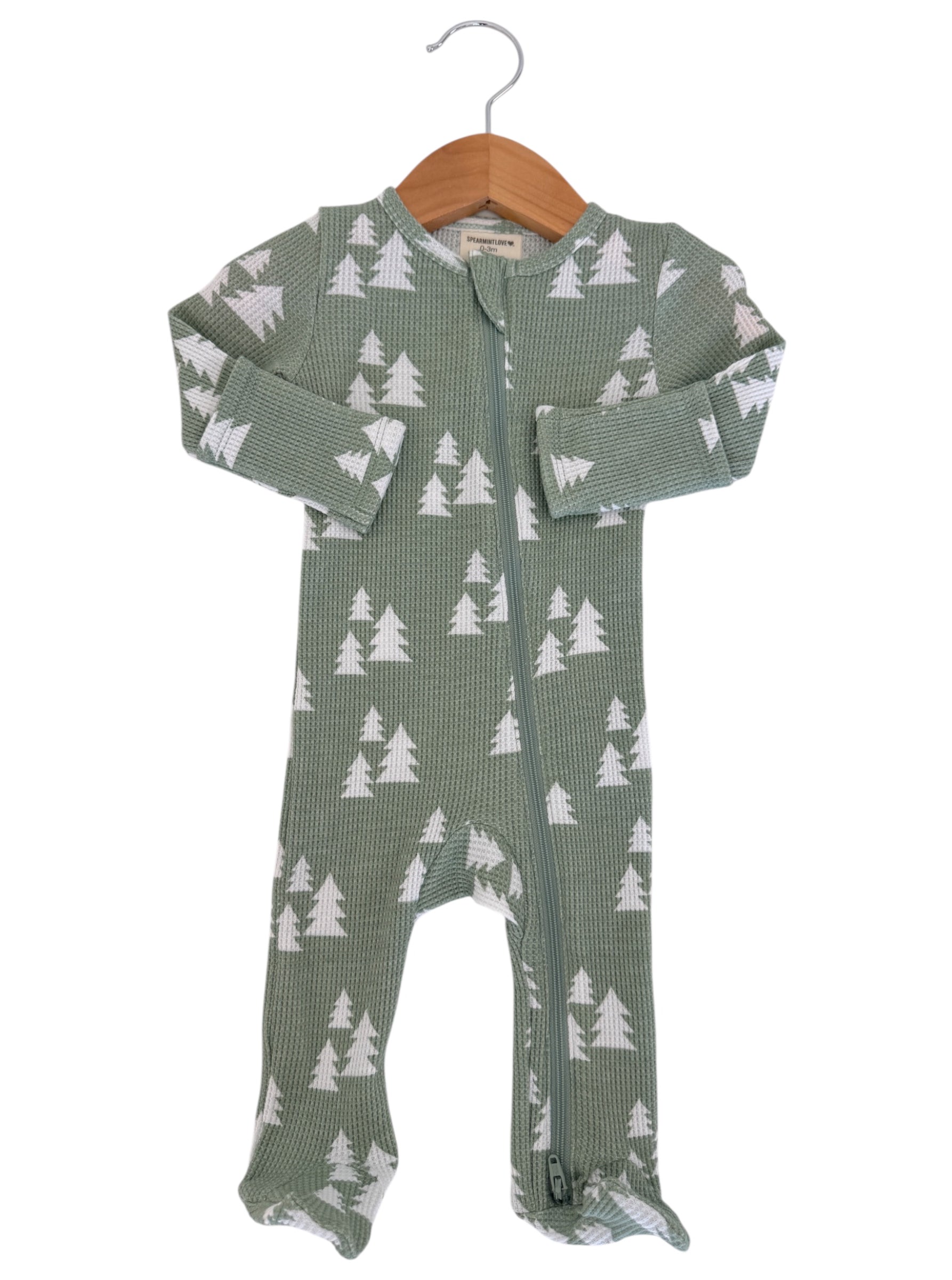 Green infant onesie with white tree patterns, featuring a full front zipper and long sleeves, hanging on a wooden hanger.