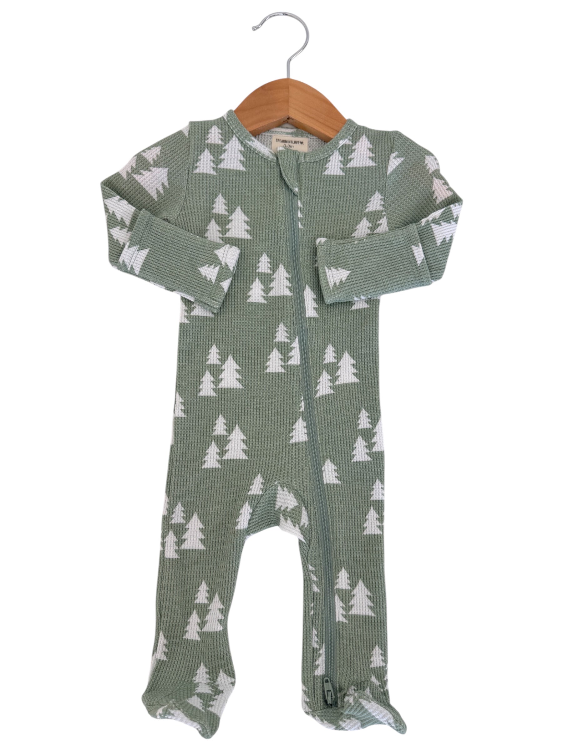 Green infant onesie with white tree patterns, featuring a full front zipper and long sleeves, hanging on a wooden hanger.