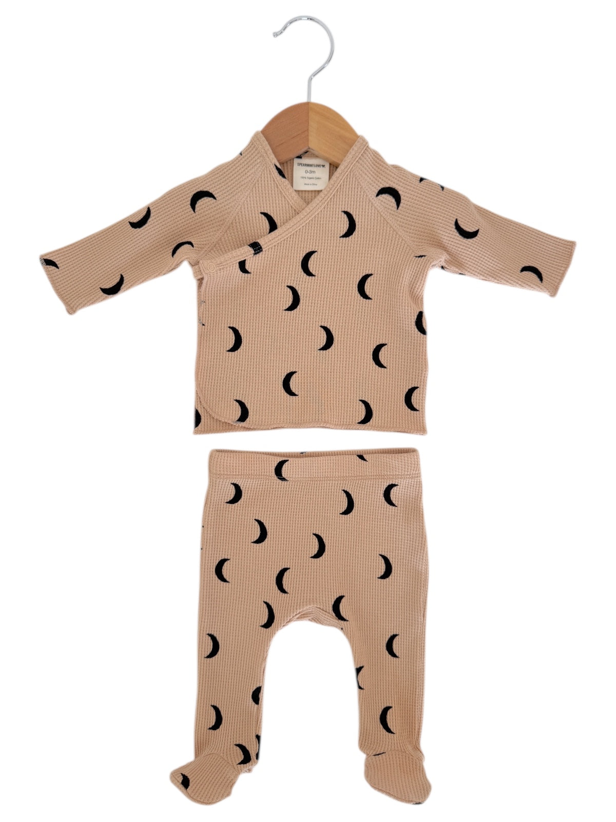 Beige baby outfit with black crescent moon pattern; includes a wrap top and footed pants, displayed on a hanger.