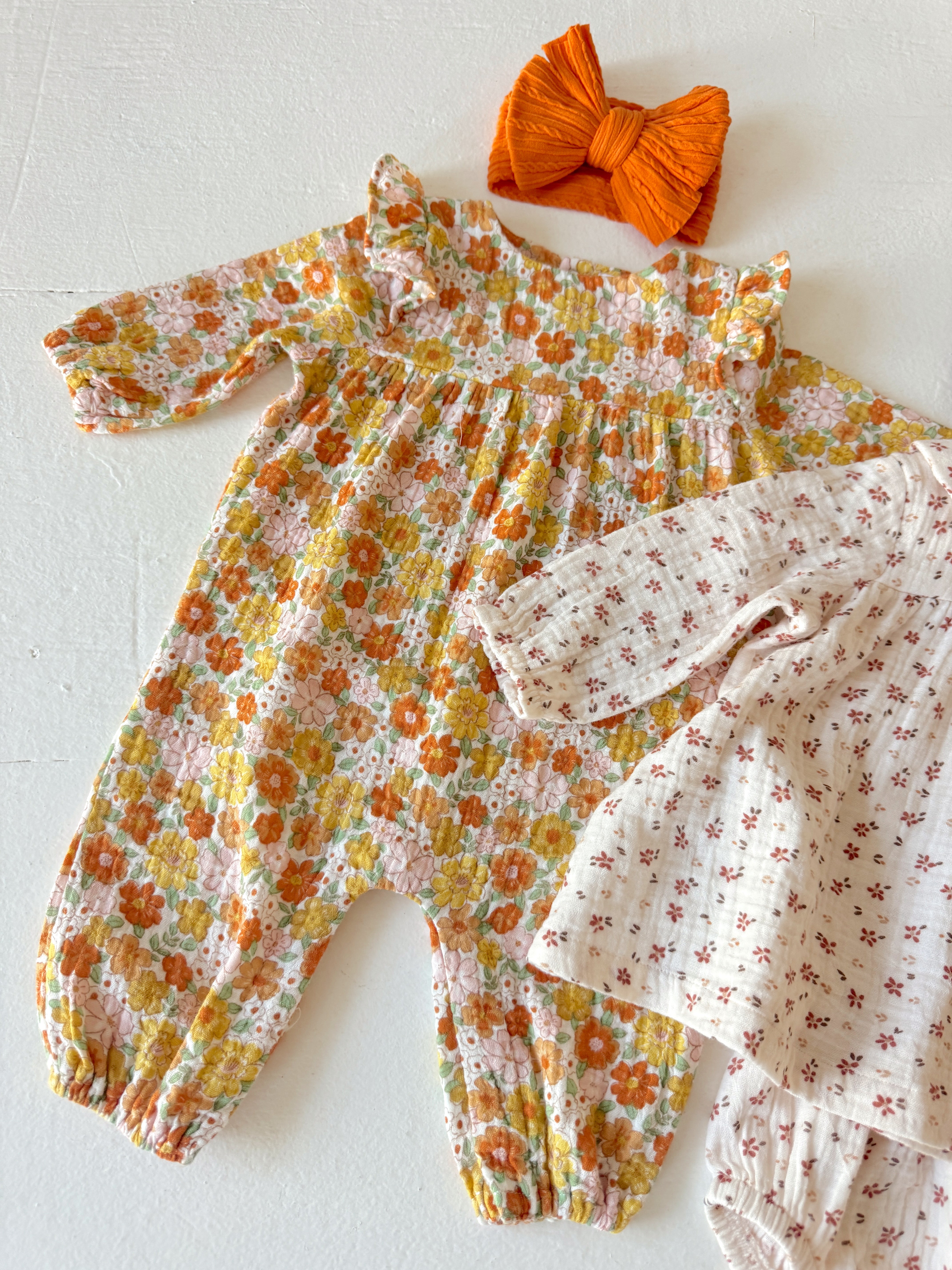 Floral baby romper and cream blouse with red flowers, paired with an orange bow headband on a white background.