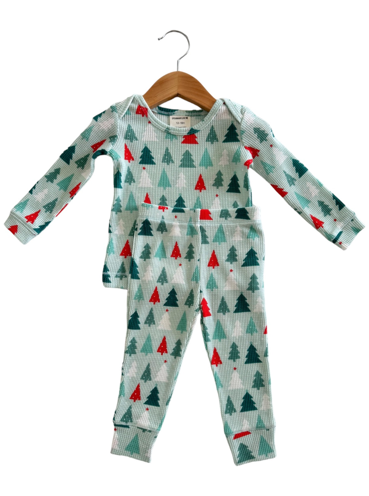 Child's holiday-themed pajama set featuring green and red trees on a light background, displayed on a hanger.