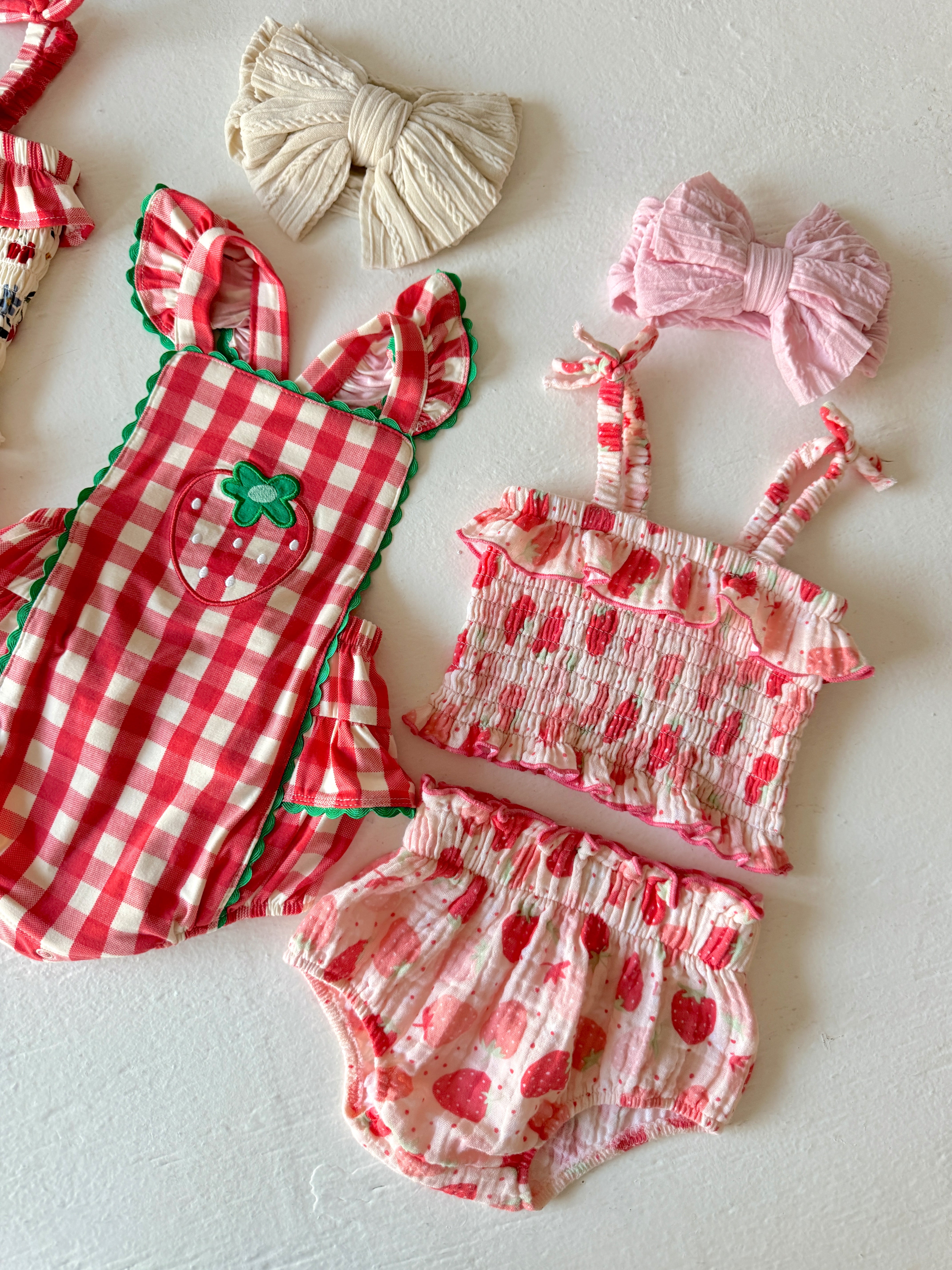 Colorful child's clothing including strawberry-themed outfits and bows on a light background.