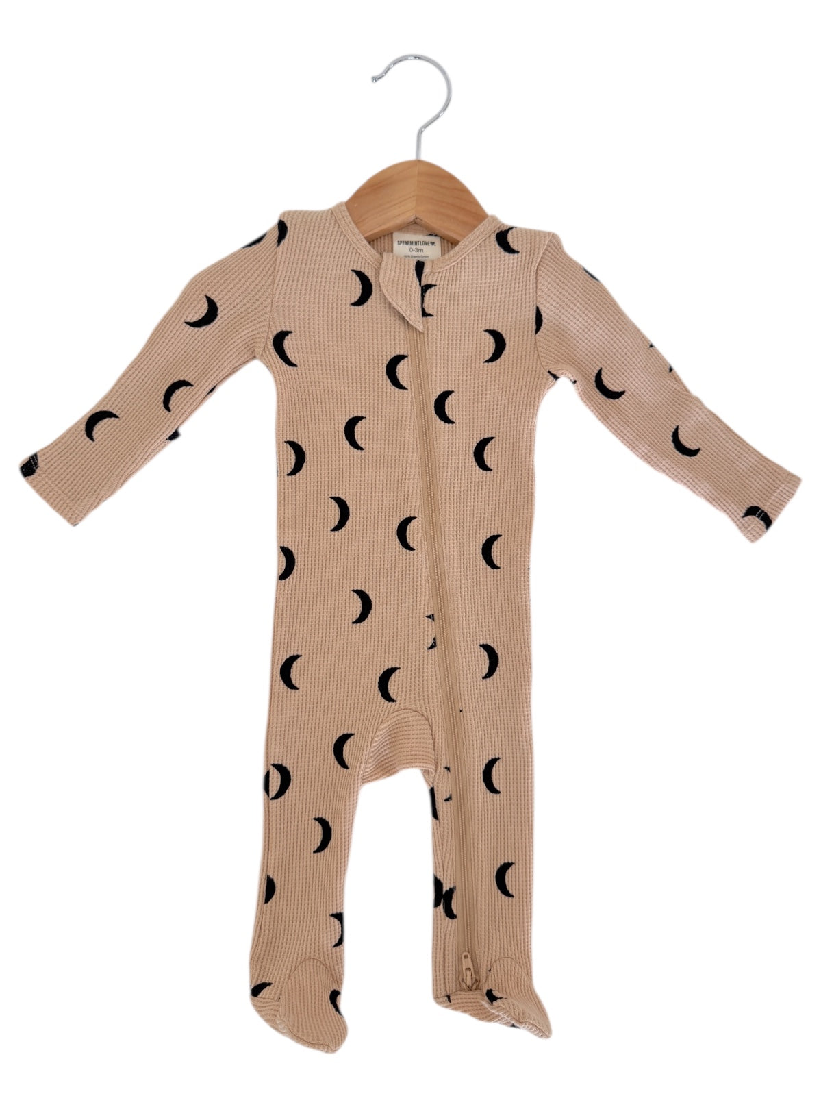 Beige baby onesie with black crescent moon patterns, displayed on a wooden hanger.