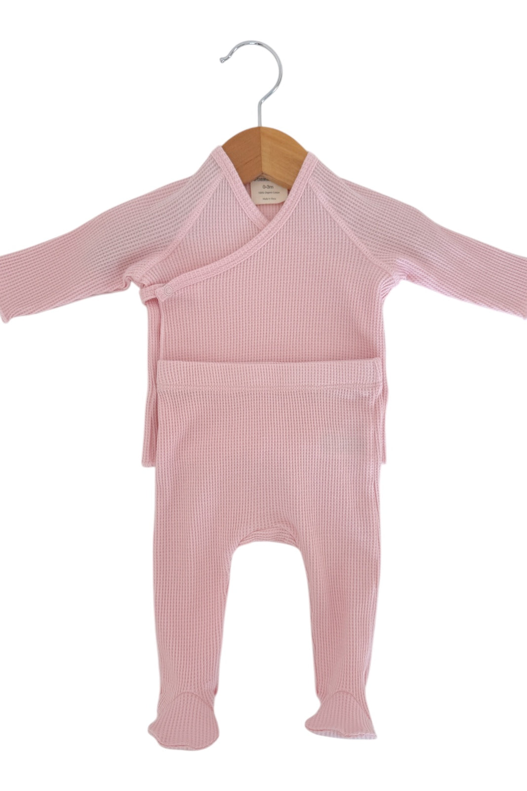 Baby pink wrap-style outfit with long sleeves and footed pants, hanging on a wooden hanger.