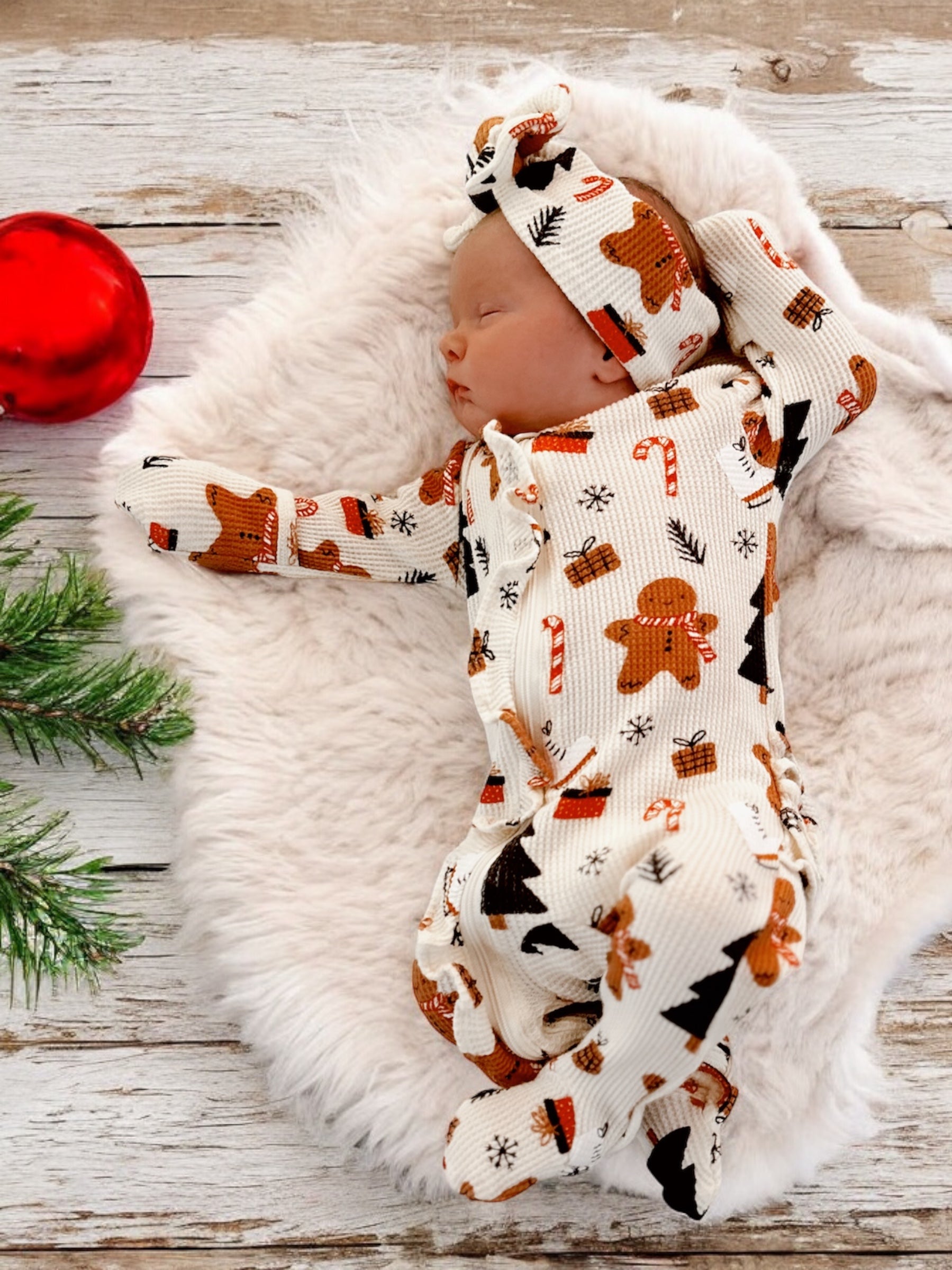 Newborn sleeping on a soft blanket, wearing festive gingerbread-themed pajamas and a matching headband.
