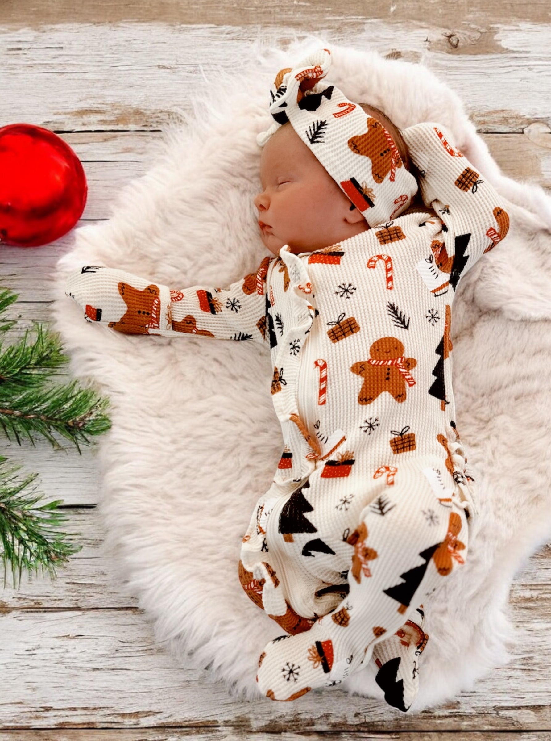 Newborn sleeping on a soft blanket, wearing festive gingerbread-themed pajamas and a matching headband.