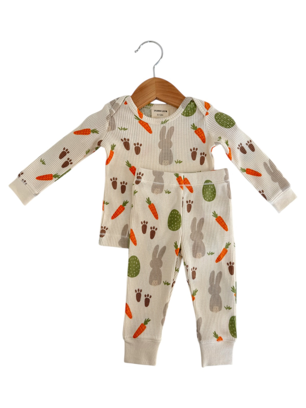 Children's pajama set featuring bunnies, carrots, and paw prints on a light background, displayed on a hanger.