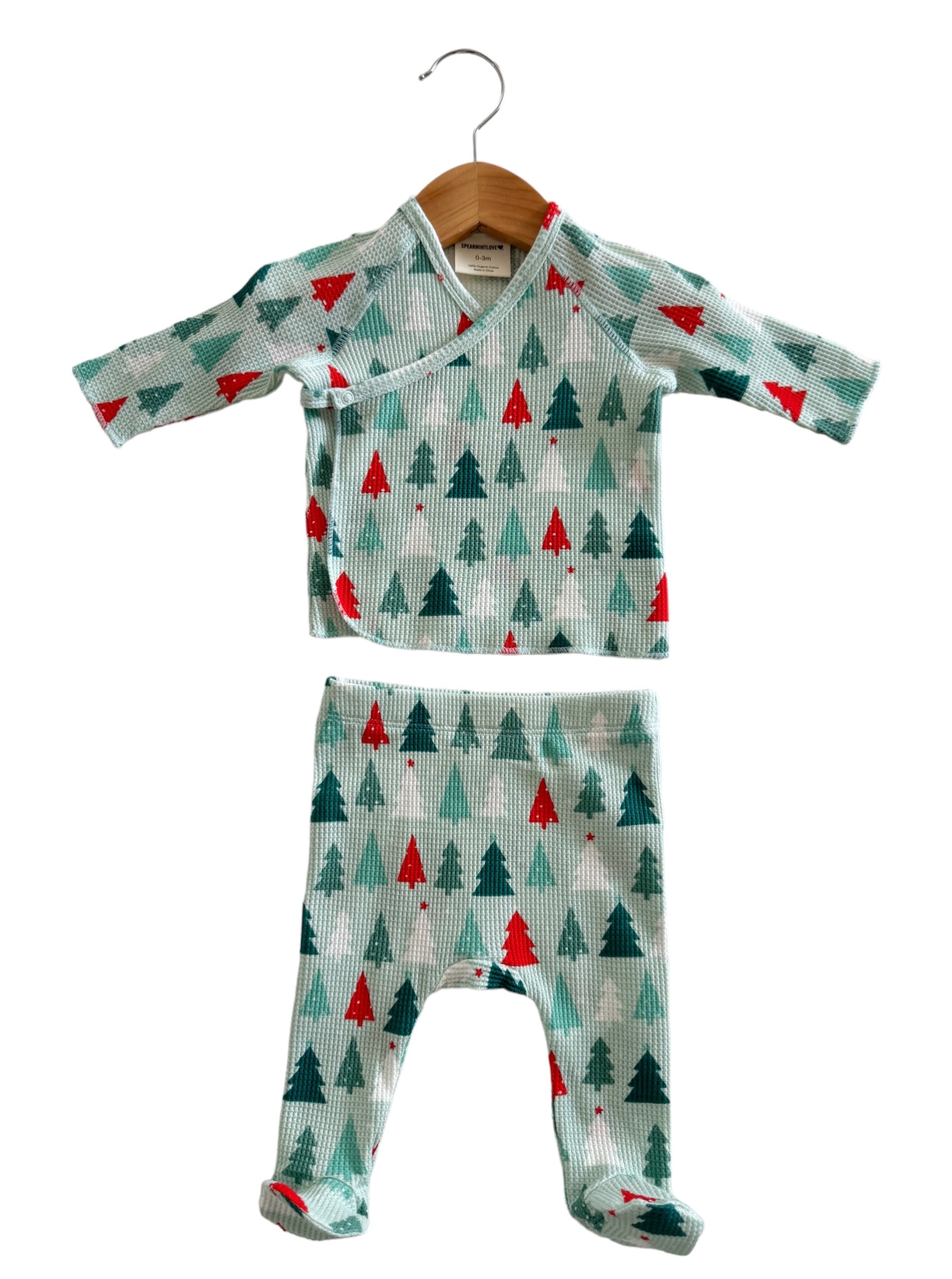 Light blue baby outfit with red and green Christmas trees, including a top and matching pants, hanging on a wooden hanger.