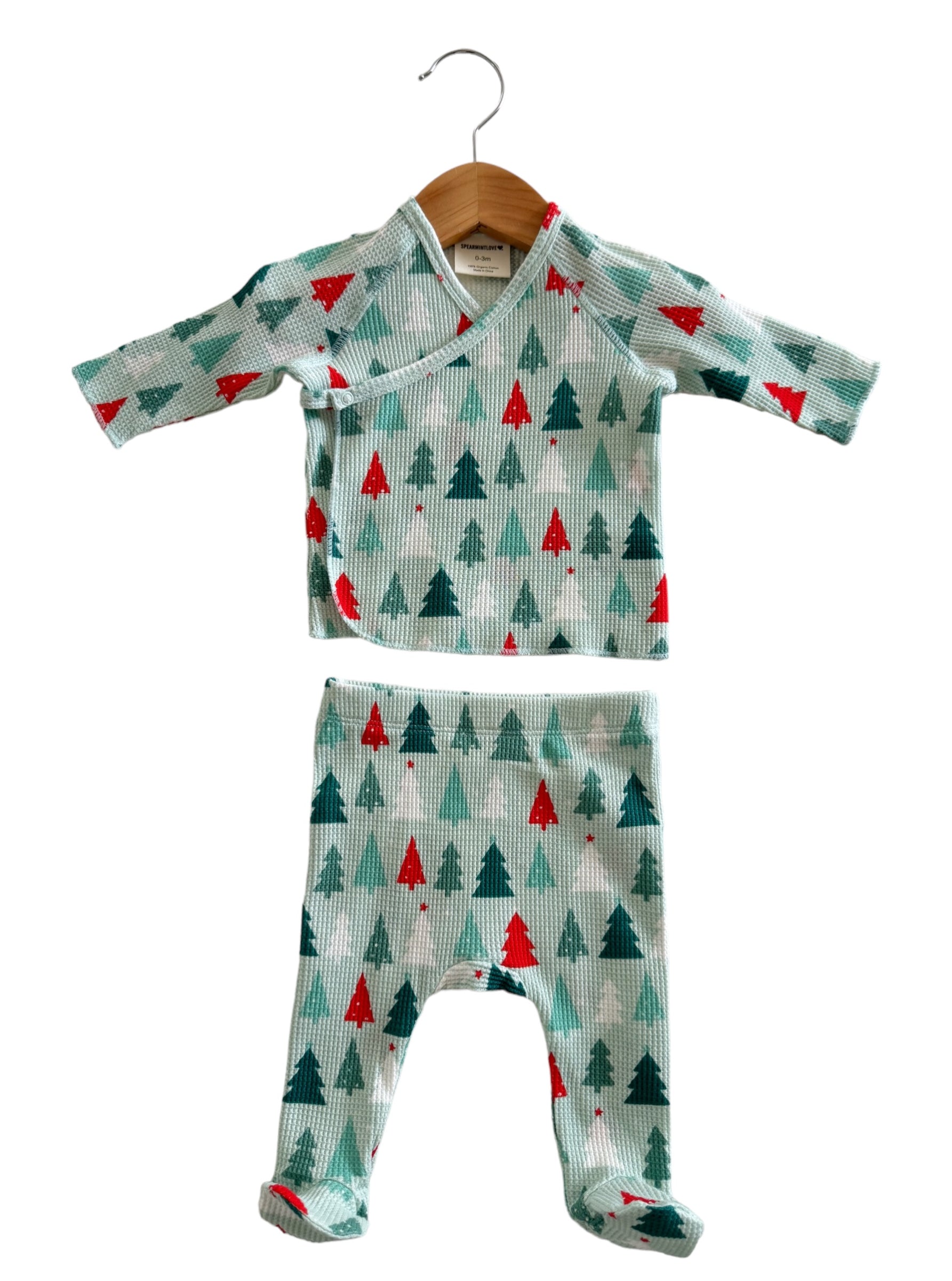 Light blue baby outfit with red and green Christmas trees, including a top and matching pants, hanging on a wooden hanger.