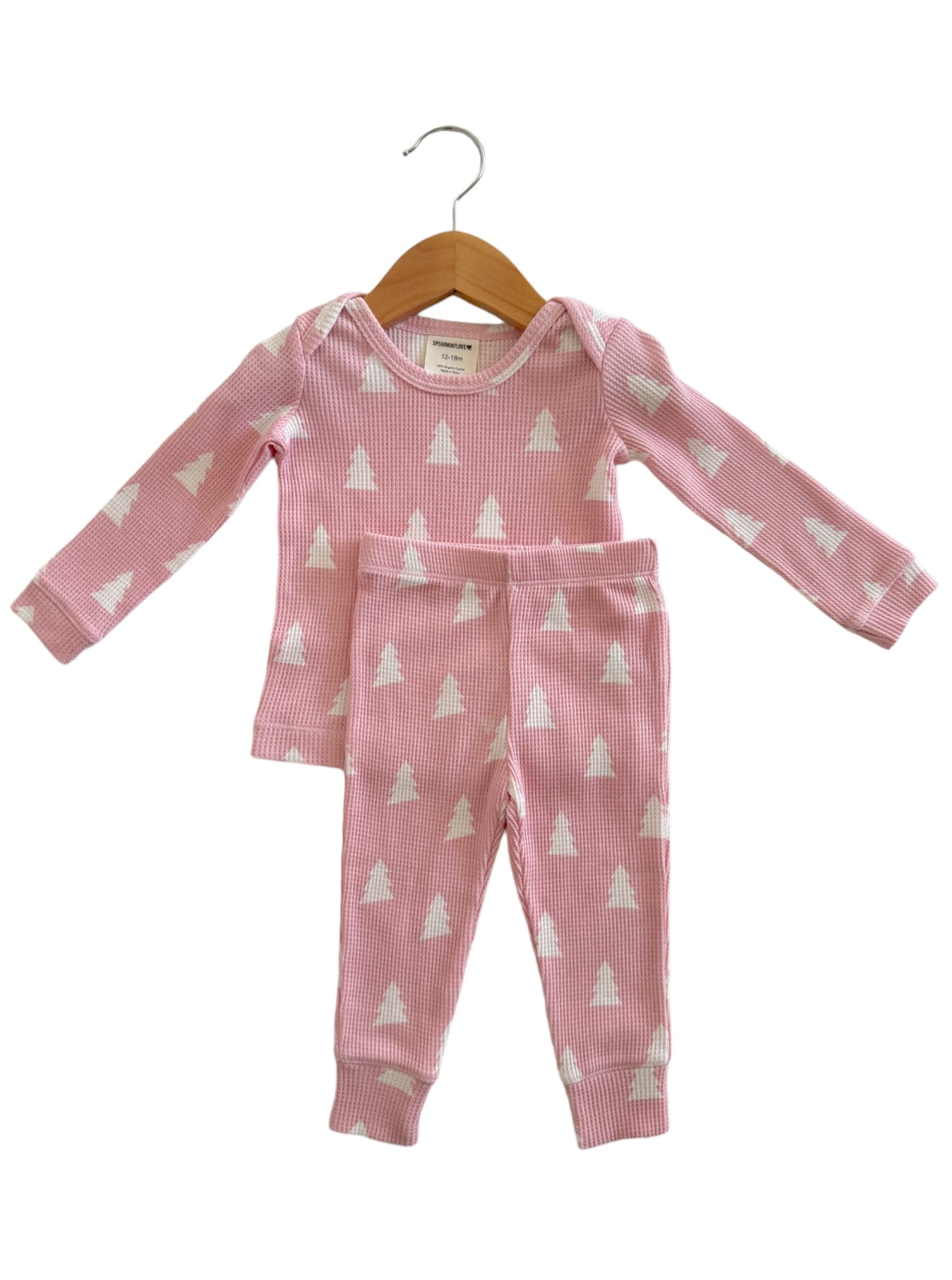Pink toddler pajamas with white tree patterns, featuring long sleeves and matching pants, displayed on a wooden hanger.