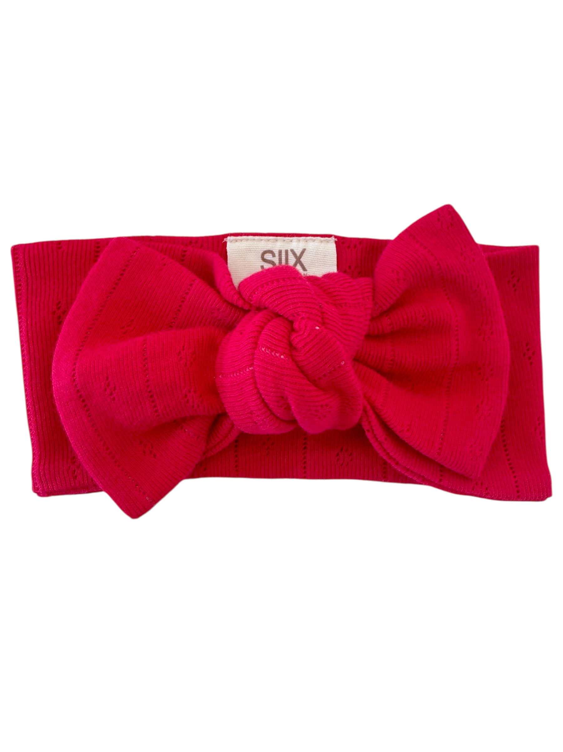 Bright pink headband with a large knot detail, featuring a textured ribbed design and a small tag marked "SIX."