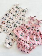 Two infants' outfits featuring playful golf cart patterns: a romper and a pink dress with matching bloomers.