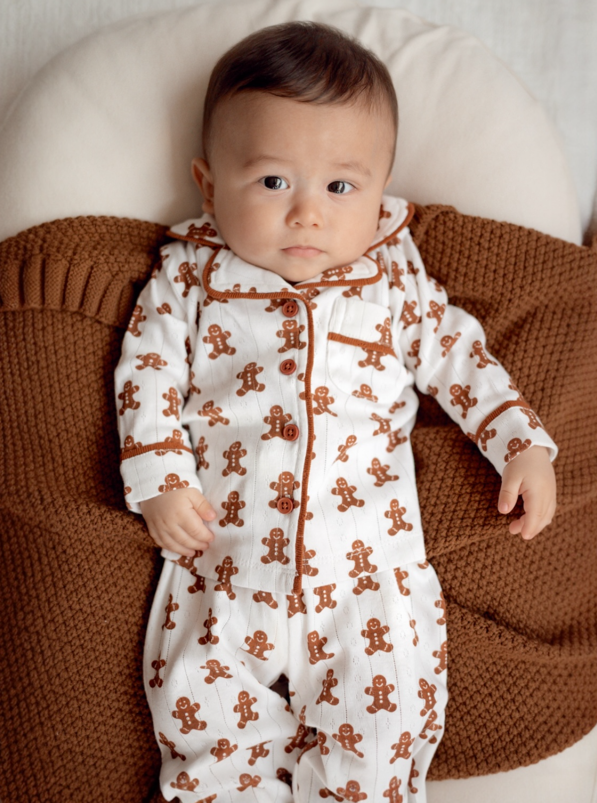 Baby in gingerbread-themed pajamas lying on a cozy, textured blanket.