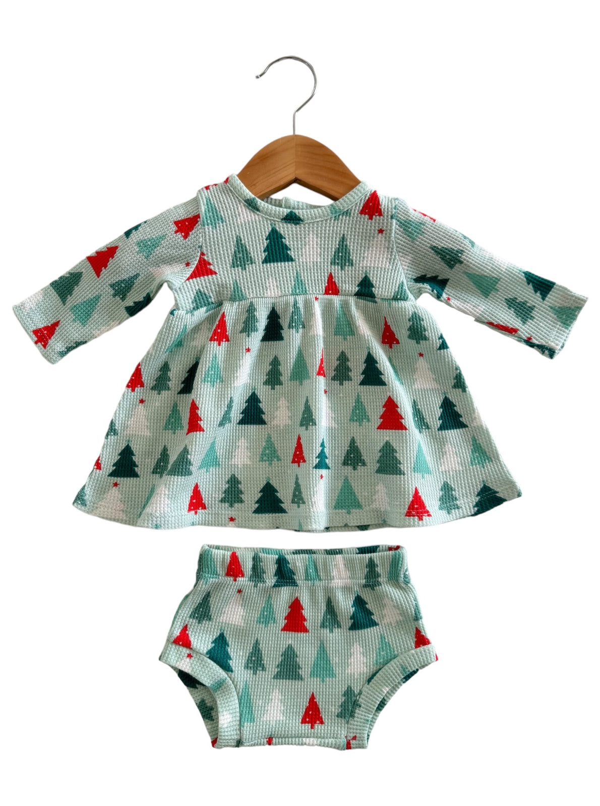 Light blue dress with green and red trees, paired with matching bloomers, hanging on a wooden hanger.