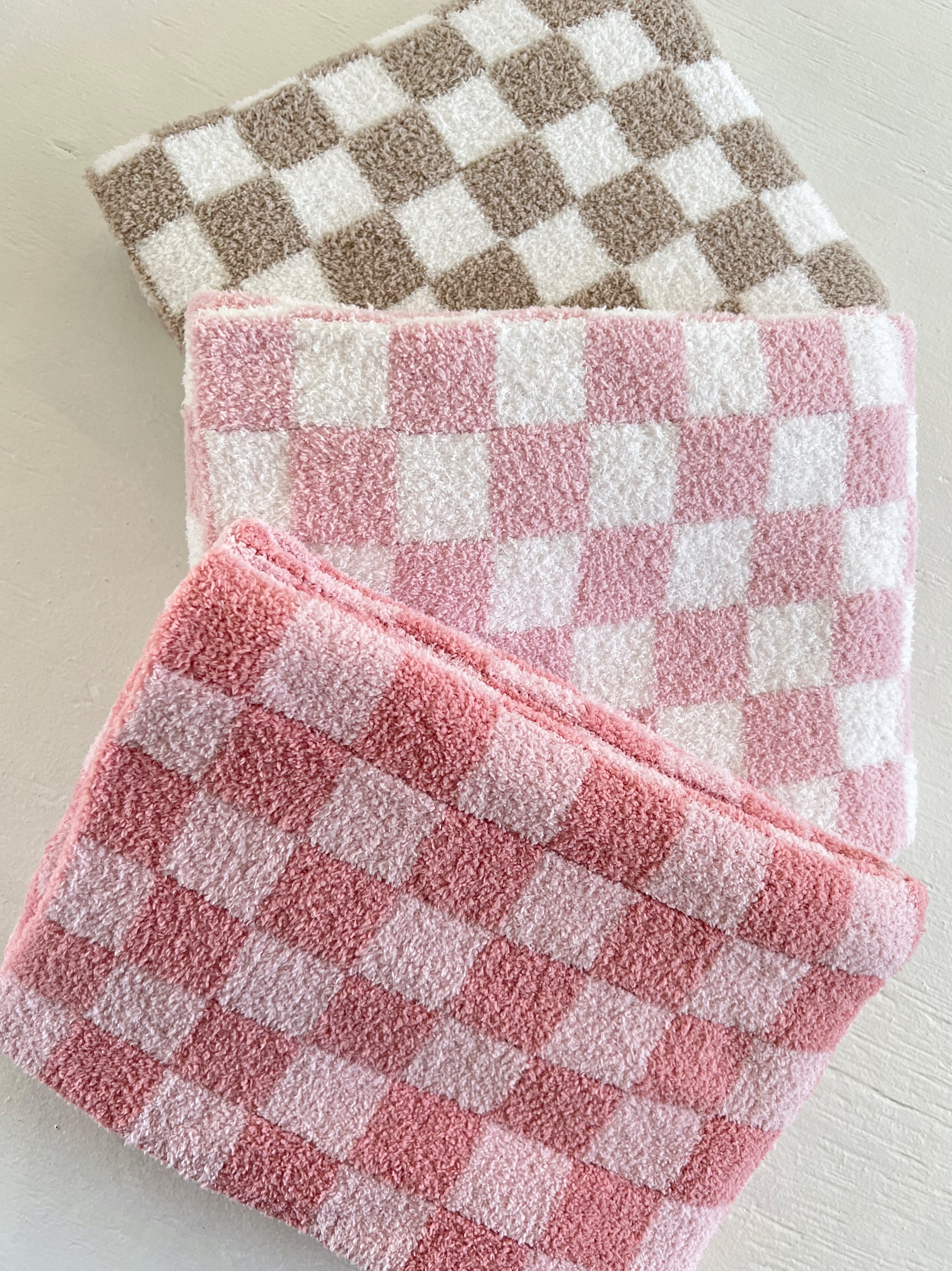 Three soft, checkered towels in shades of pink and brown arranged on a light surface.