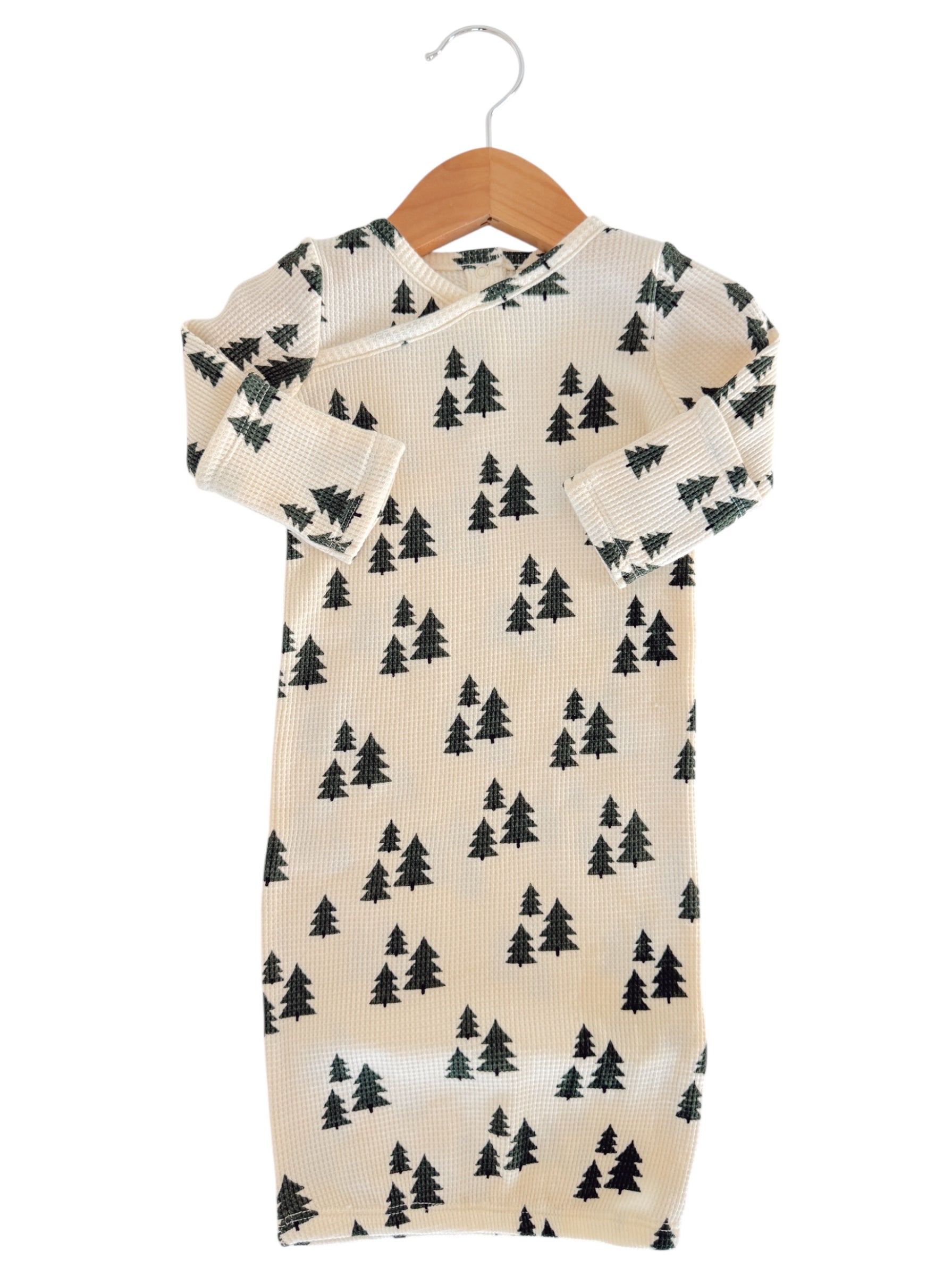 Infant outfit featuring a cream fabric with green tree patterns, displayed on a wooden hanger.