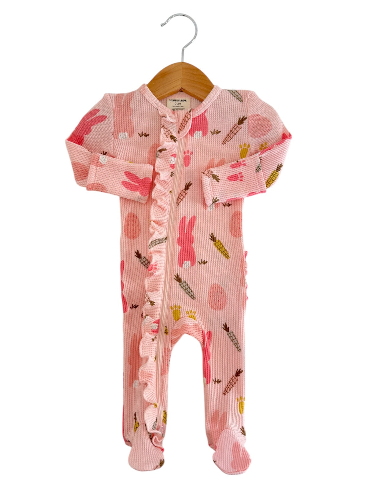 Pink baby onesie with bunny patterns, ruffled details, and footed design, displayed on a wooden hanger.