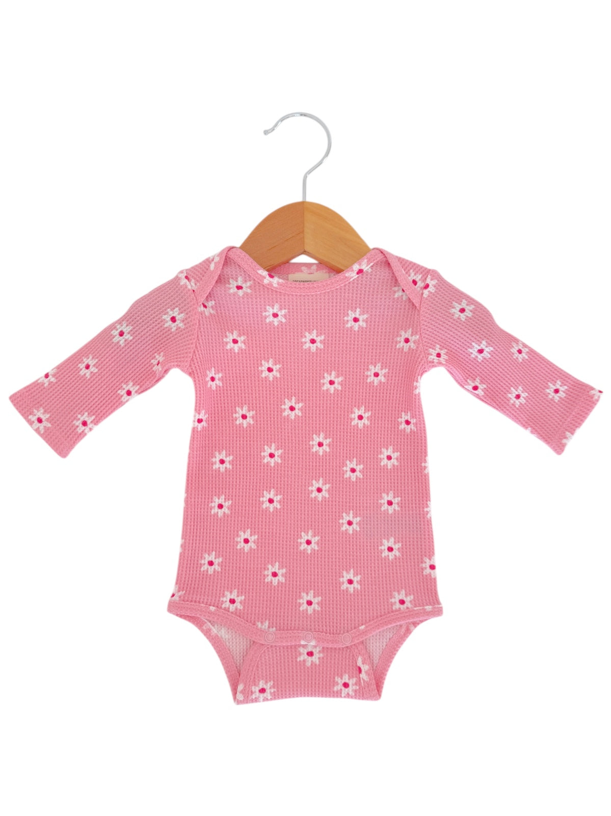 Pink baby onesie with long sleeves and floral pattern, displayed on a wooden hanger.