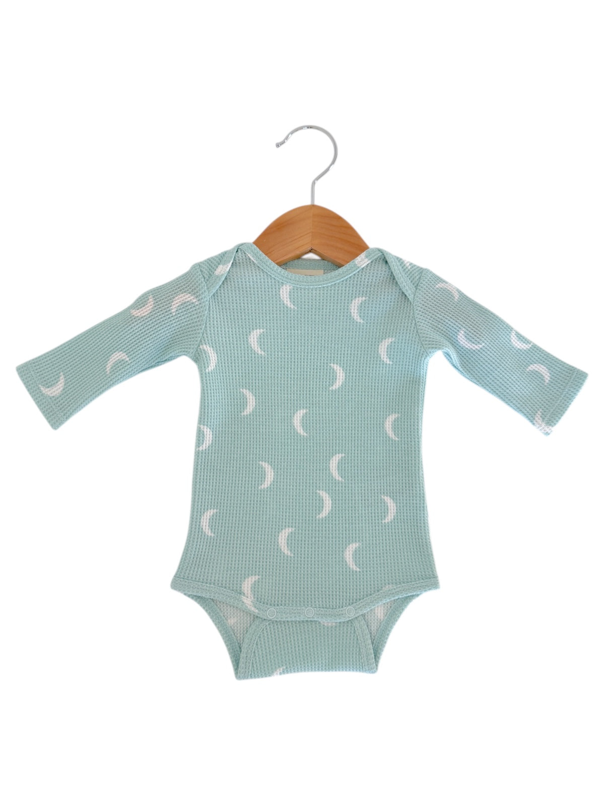 Light blue long-sleeve baby bodysuit with crescent moon patterns, displayed on a wooden hanger.