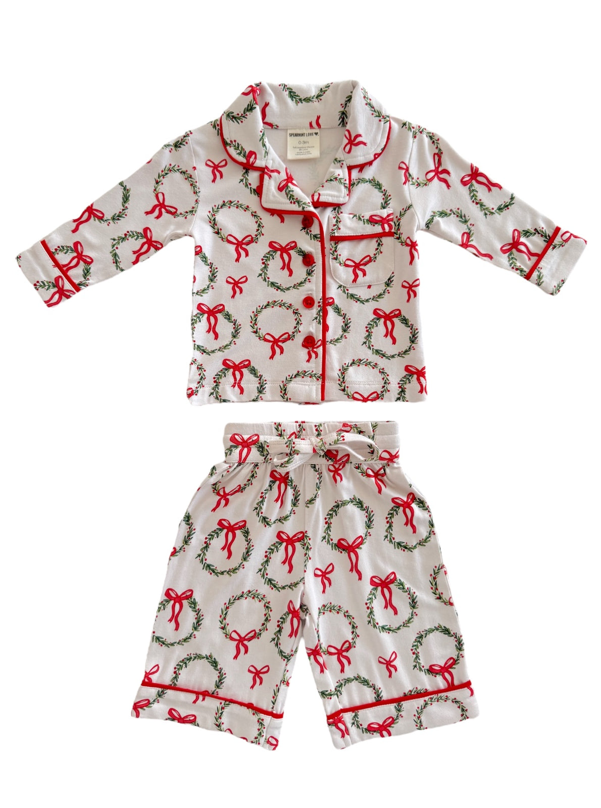 Child's festive pajama set featuring a white background, red bows, and green wreath patterns.