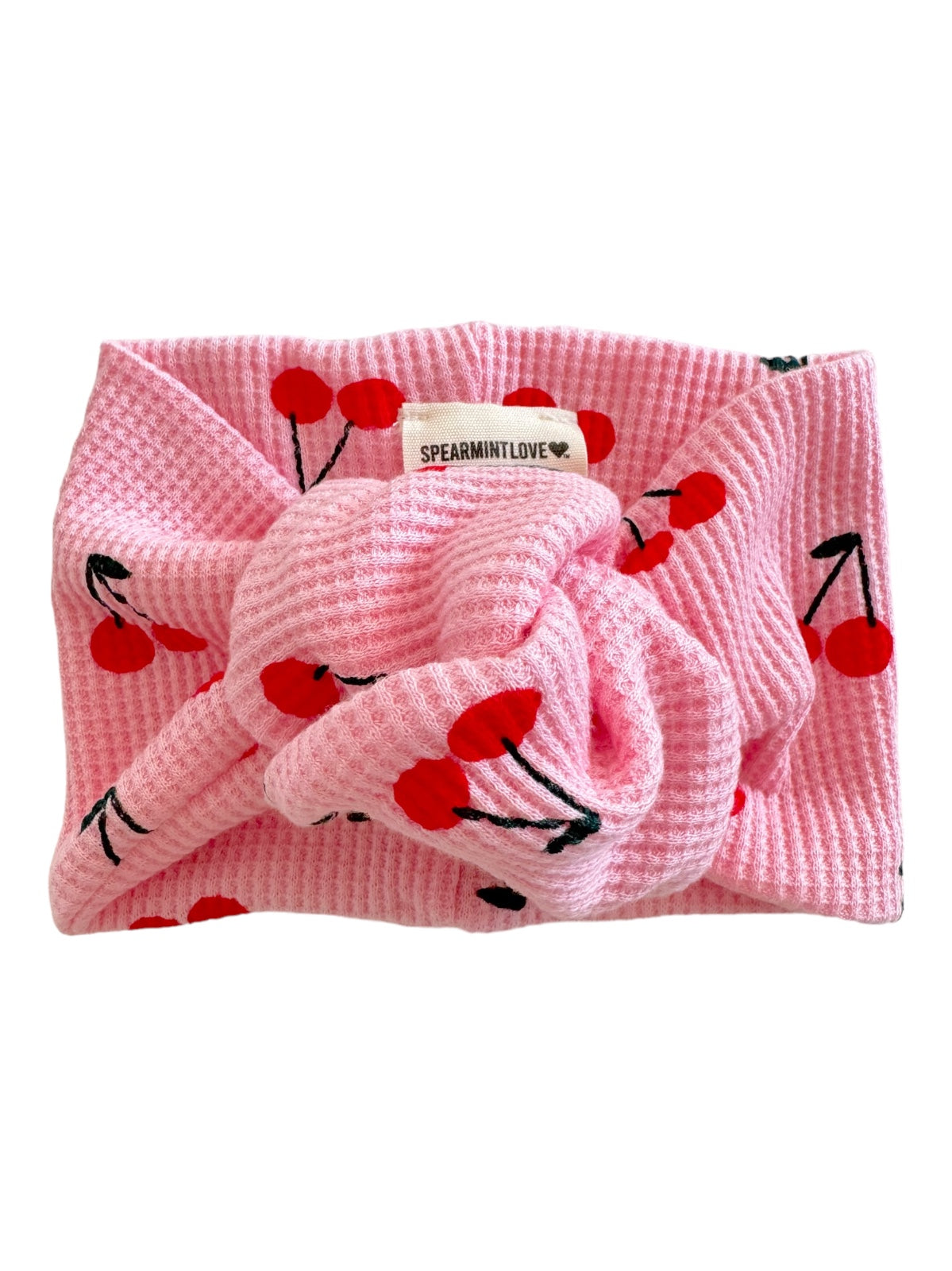 Pink headband with cherry print, featuring a knot and a tag that says "SPEARMINTLOVE."