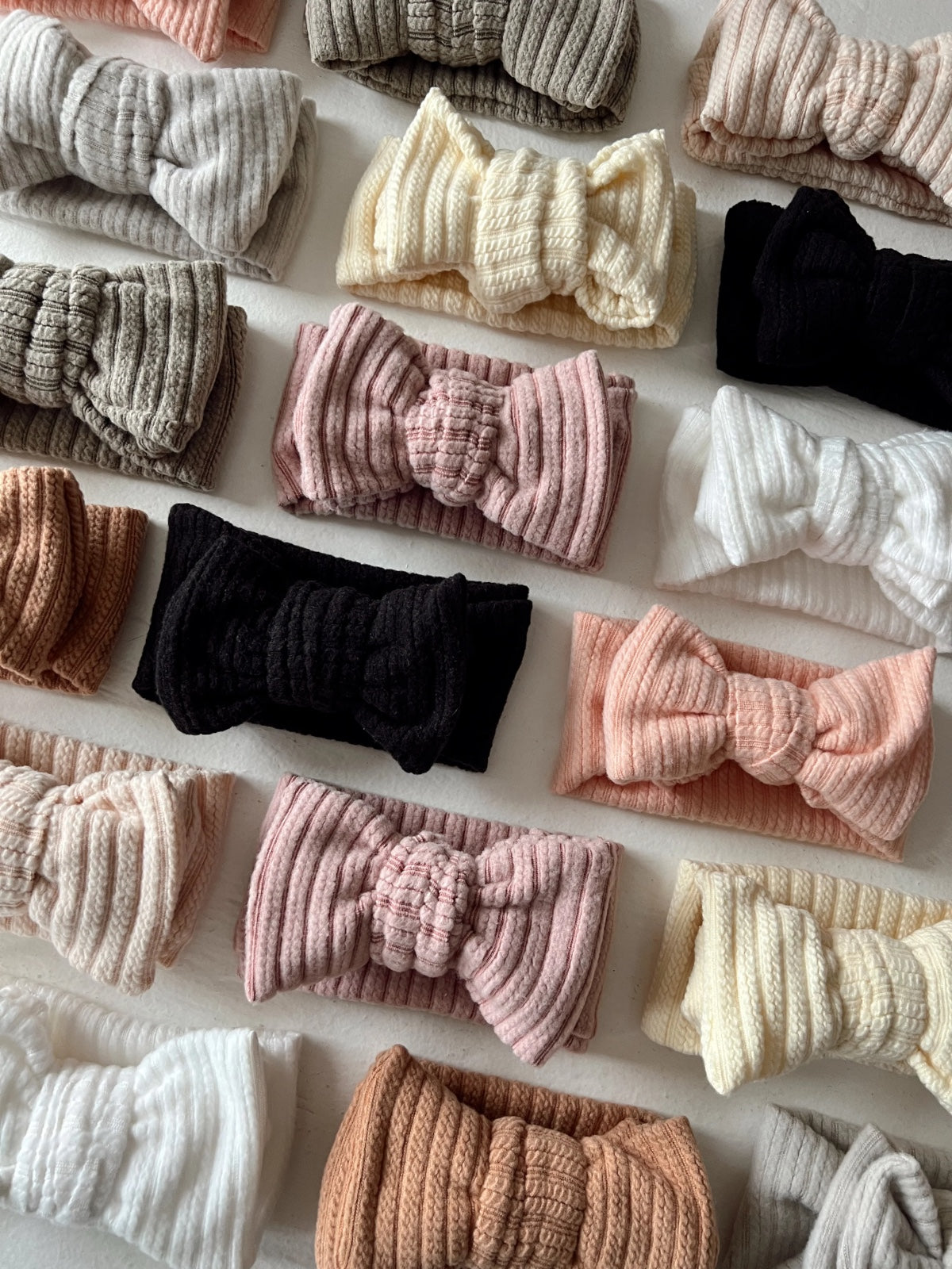 Collection of soft, textured headbands in various pastel colors arranged neatly on a light background.