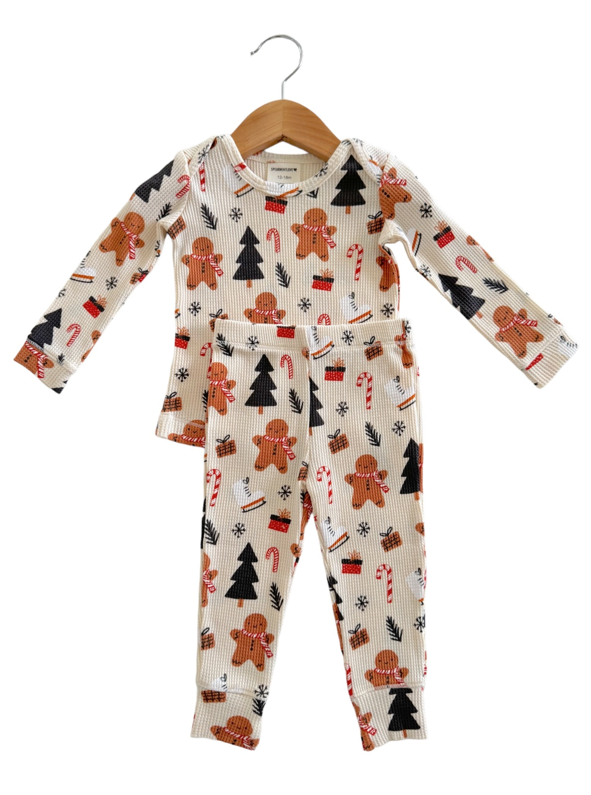 Children's holiday pajamas with gingerbread men, candy canes, and Christmas trees on a cream background.