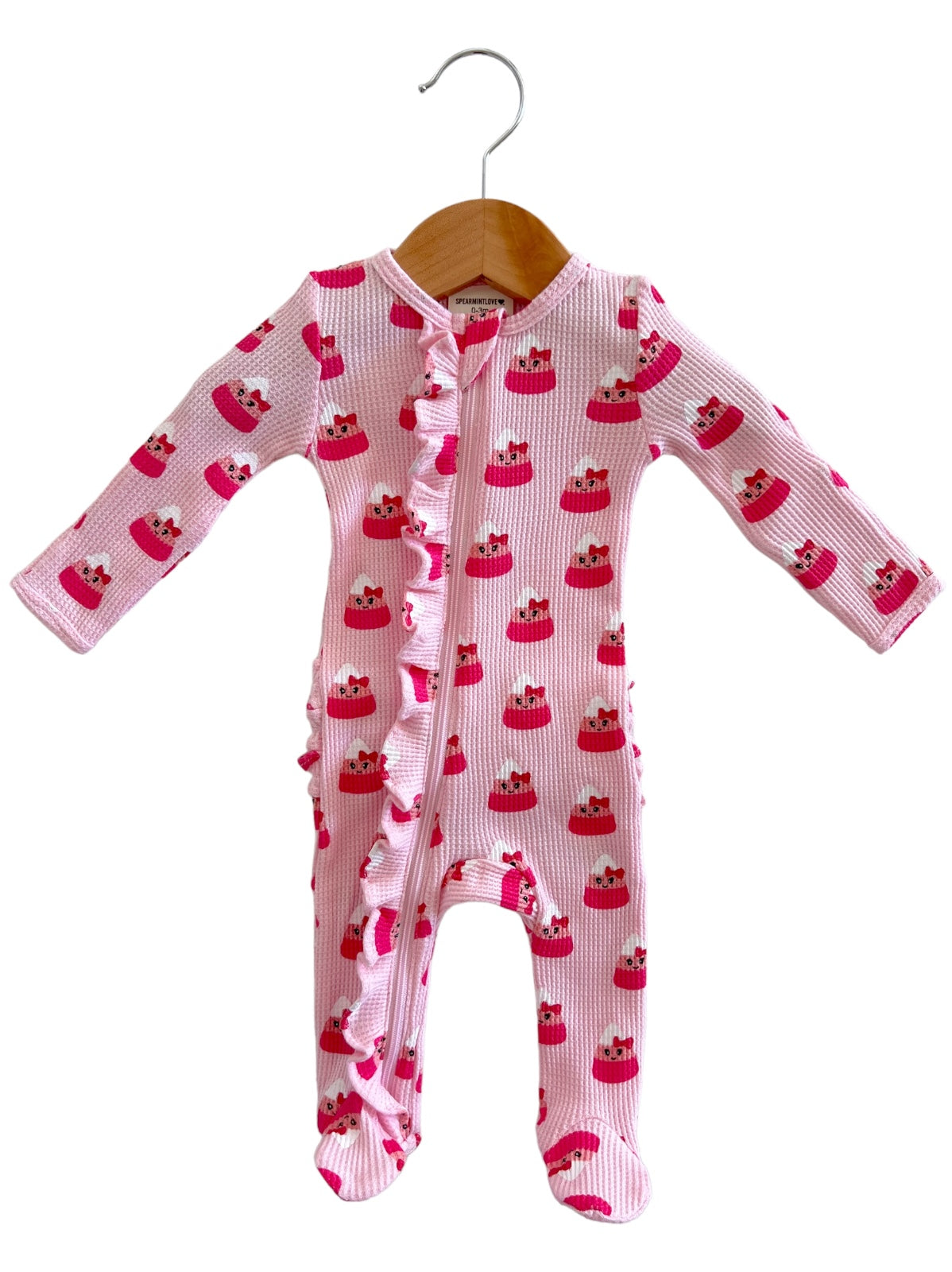Pink baby onesie with cupcake pattern, featuring a zipper and ruffled detailing on the front. Hanging on a wooden hanger.