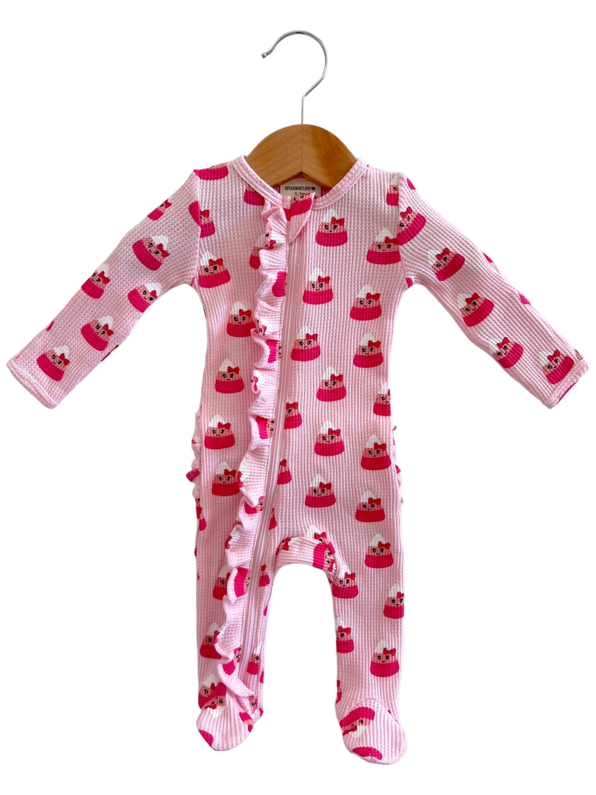 Pink baby onesie with cupcake pattern, featuring a zipper and ruffled detailing on the front. Hanging on a wooden hanger.