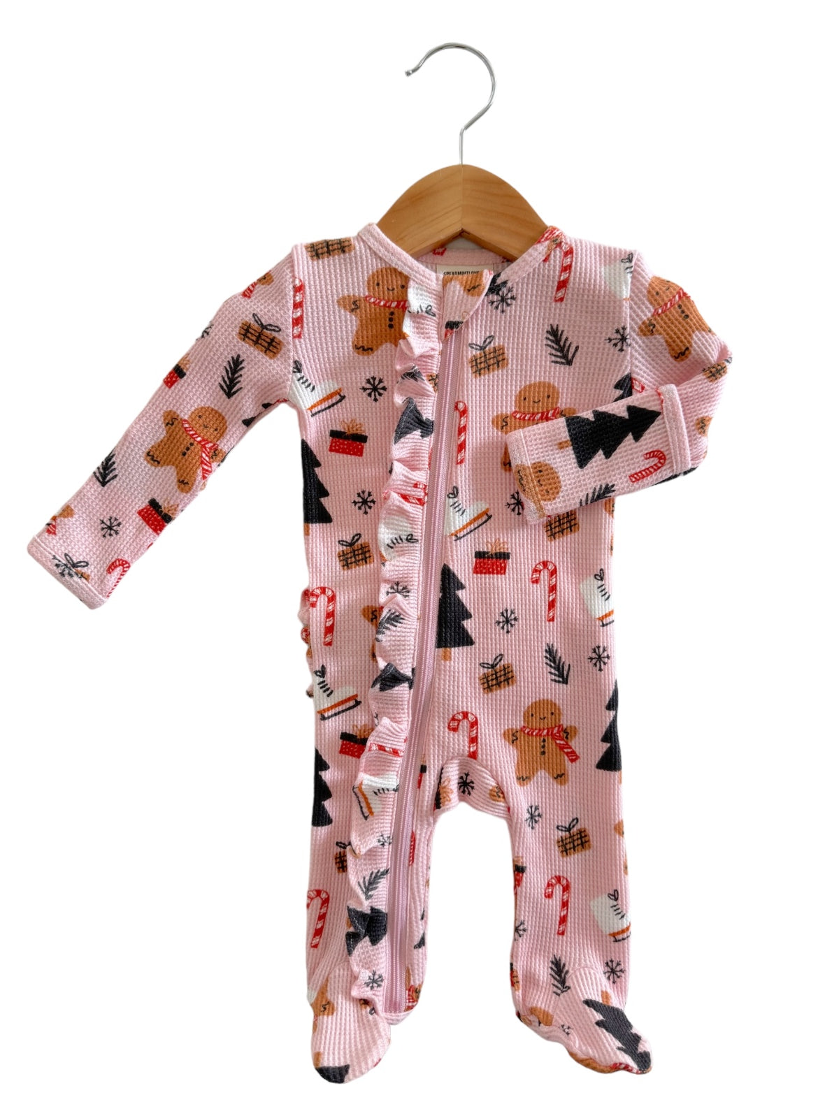 Pink children's onesie with gingerbread, candy canes, and Christmas trees hanging on a wooden hanger.