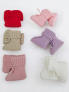 Colorful knitted infant booties in red, pink, lavender, beige, and white arranged on a white background.