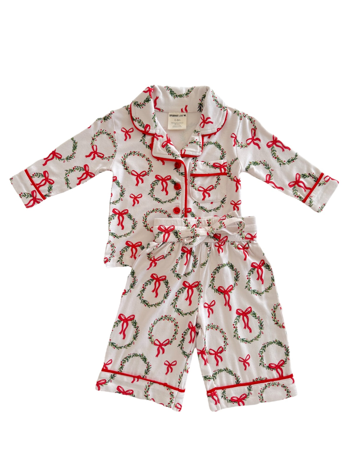 Child's holiday pajama set featuring white fabric with red bows and green wreath designs.
