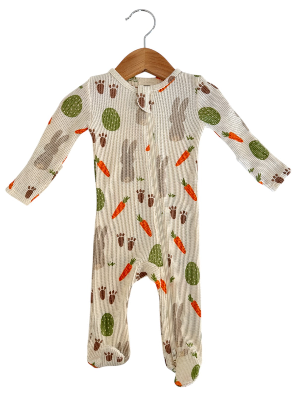 Baby onesie featuring a playful bunny and vegetable print, hanging on a wooden hanger.