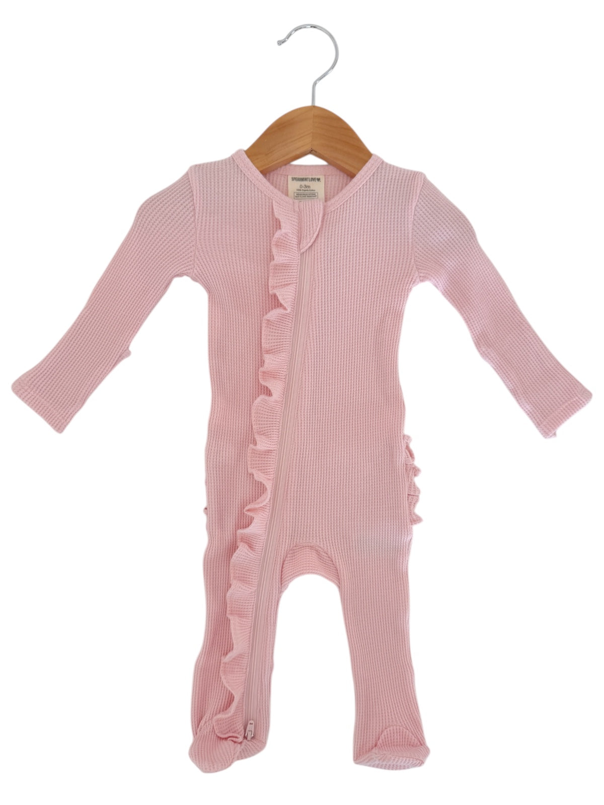 Pink baby onesie with ruffle details, featuring long sleeves and a front zipper, hanging on a wooden hanger.