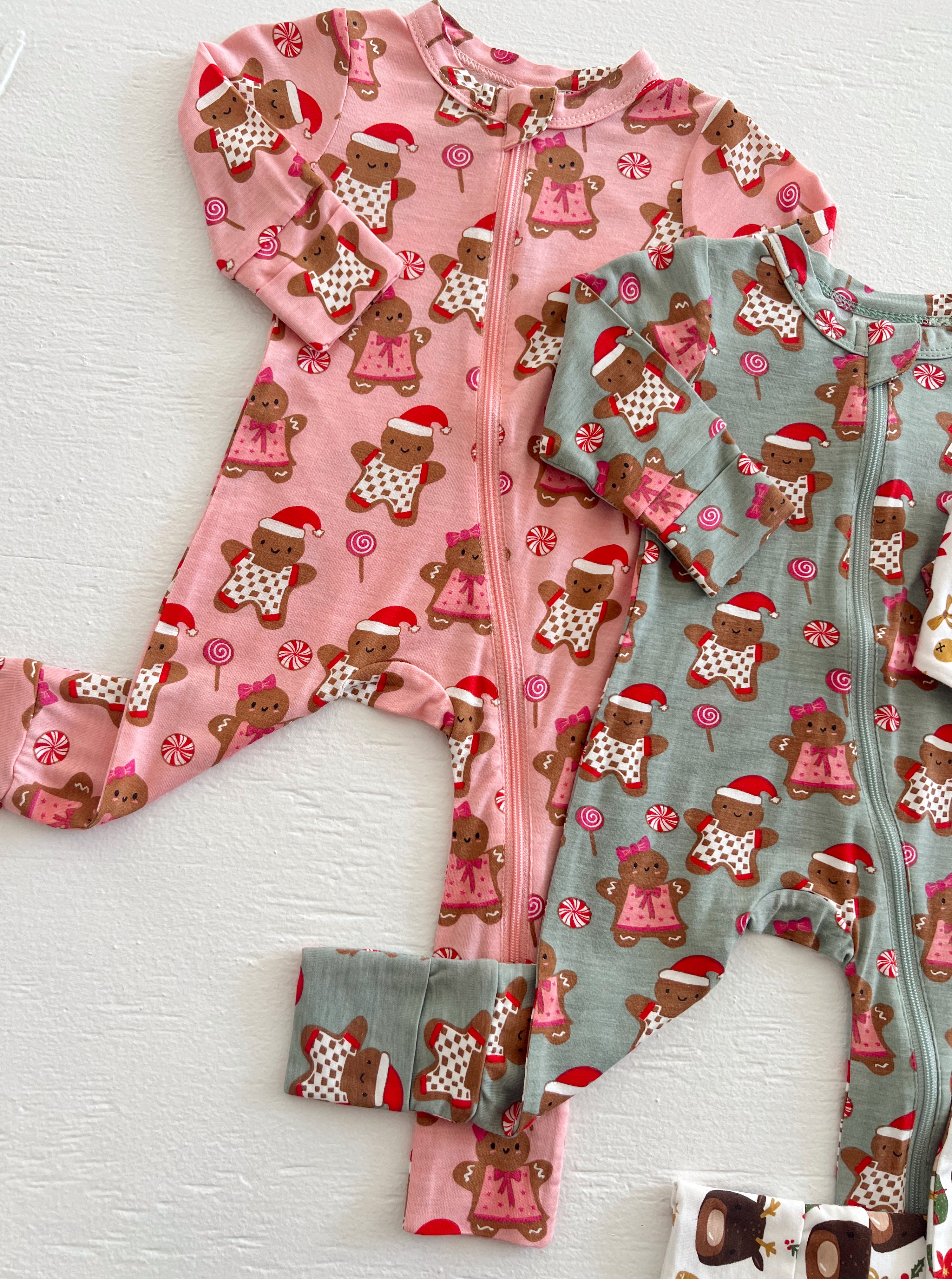 Two holiday-themed children's onesies in pink and green, featuring gingerbread figures and candy designs.