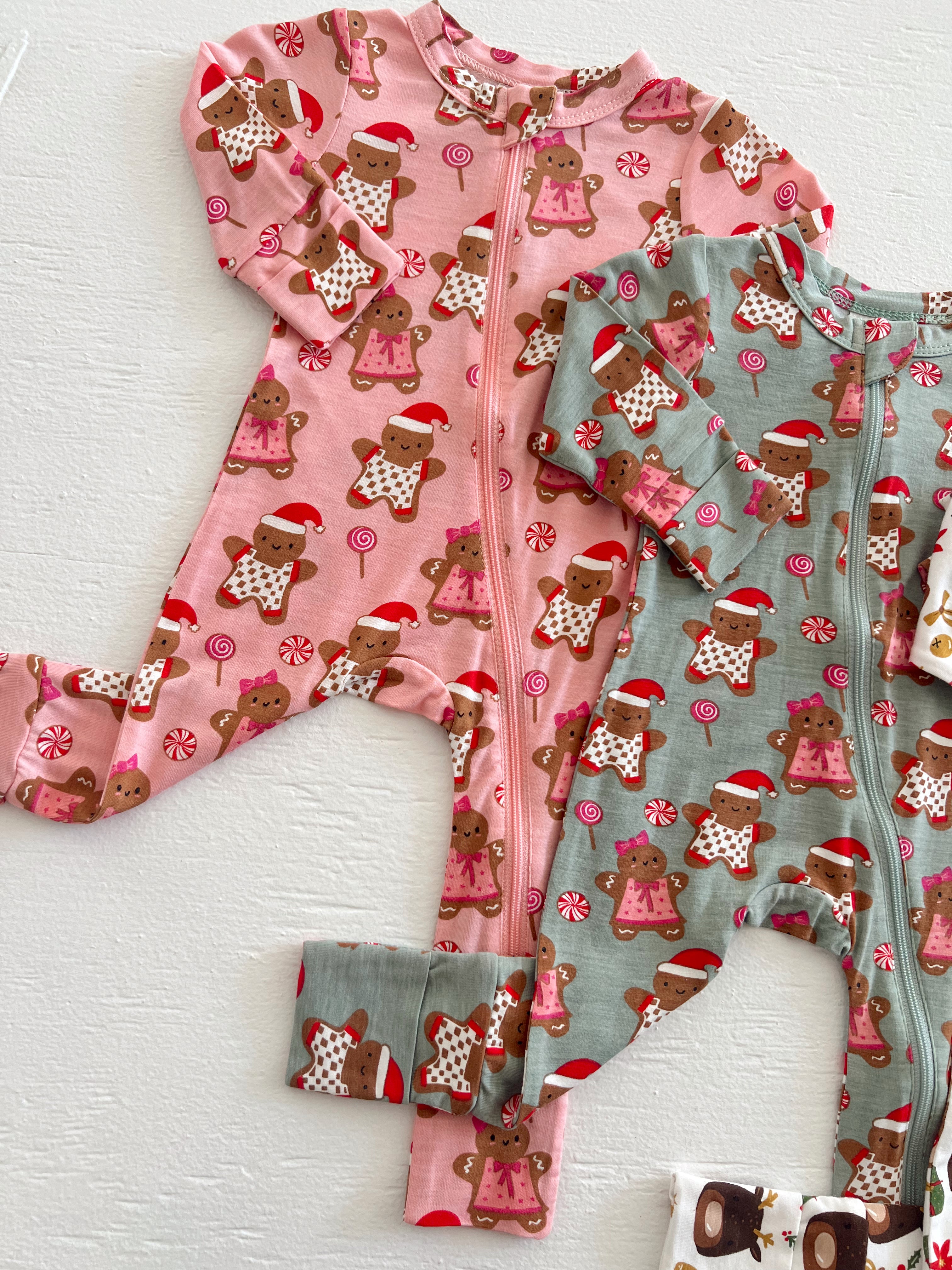 Two holiday-themed children's onesies in pink and green, featuring gingerbread figures and candy designs.