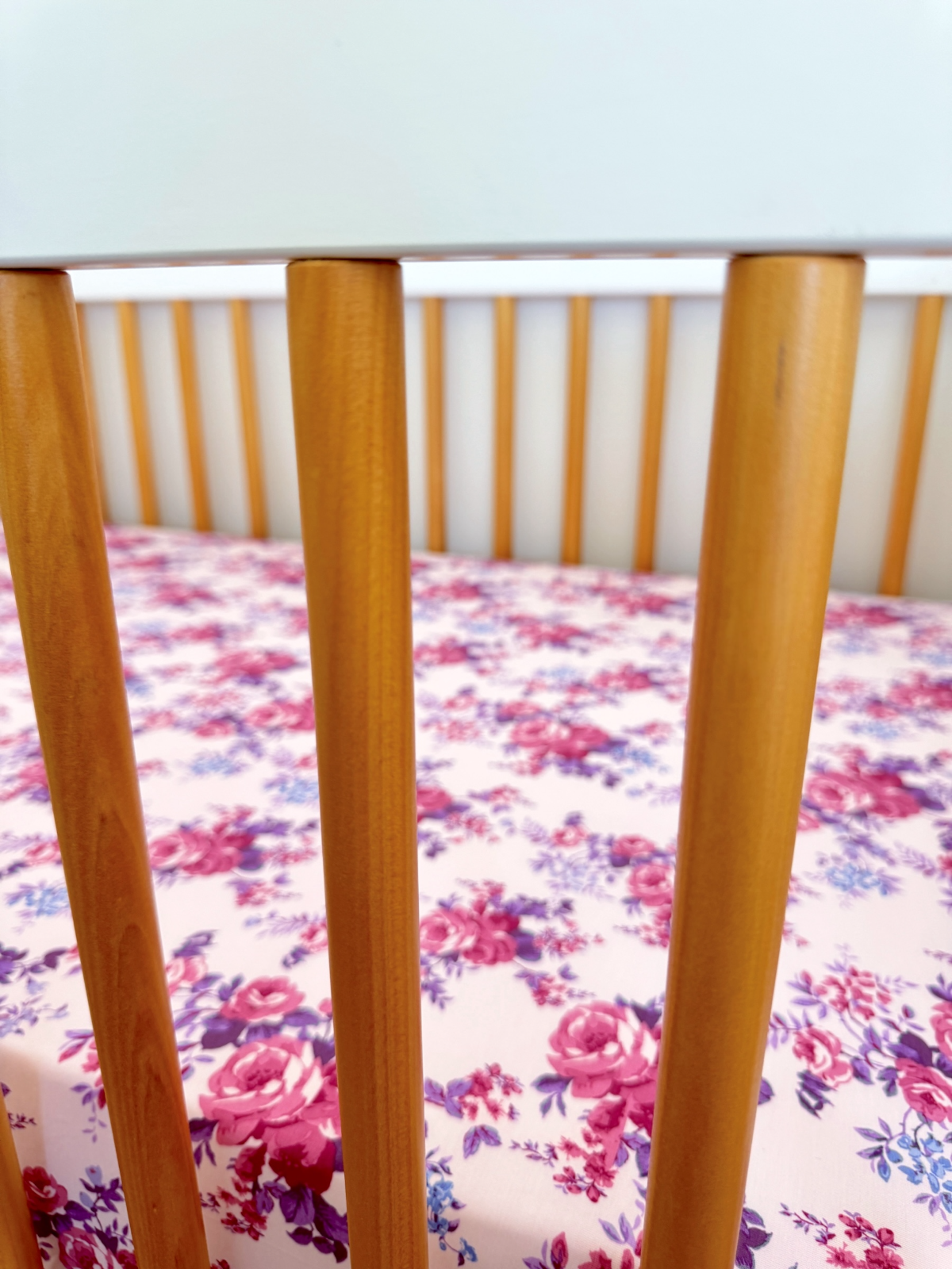 Wooden crib slats with a floral patterned mattress in shades of pink and purple.