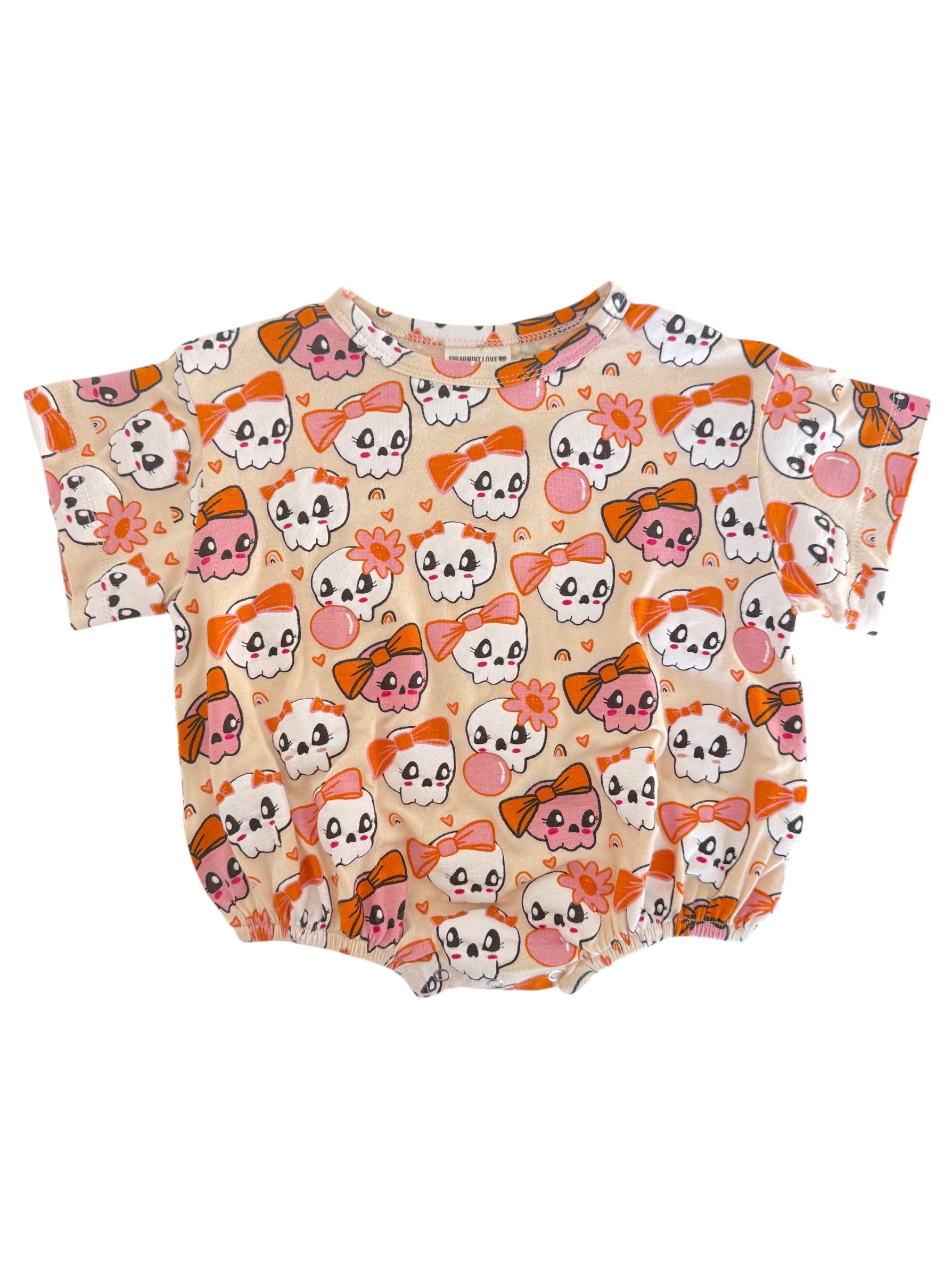 Children's short-sleeve onesie with a playful skull and bow pattern in pink and orange on a cream background.