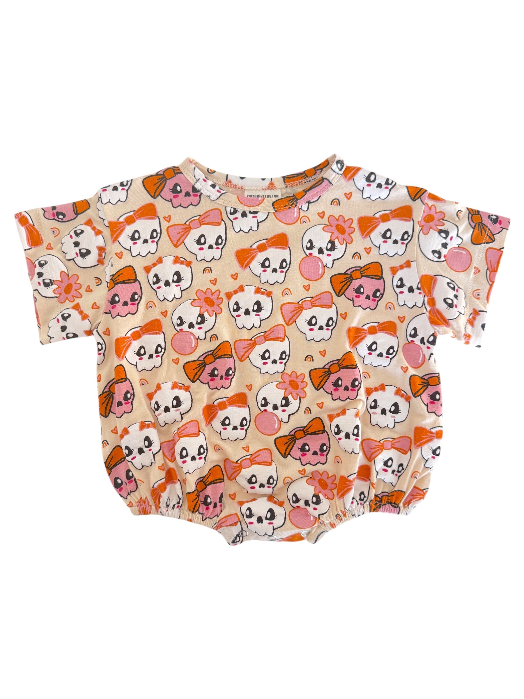 Children's short-sleeve onesie with a playful skull and bow pattern in pink and orange on a cream background.