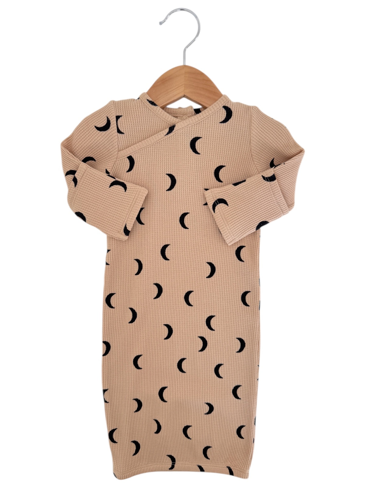 Beige ribbed baby dress with black crescent moon patterns, hanging on a wooden hanger.