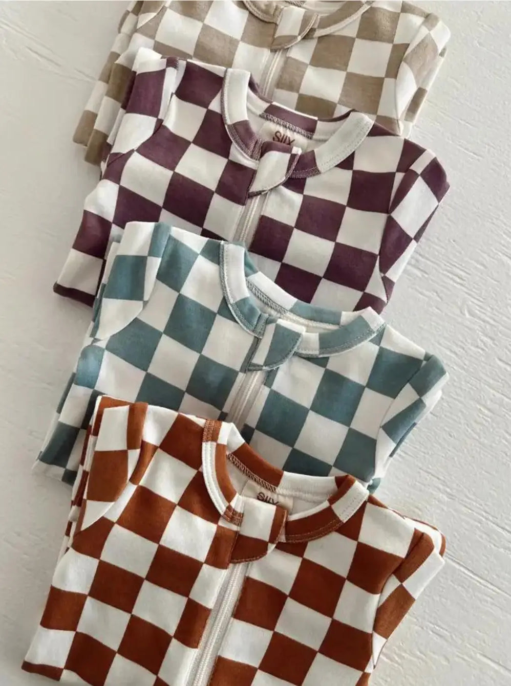 Colorful checkered zip-up pajamas stacked neatly in four different colors on a white background.