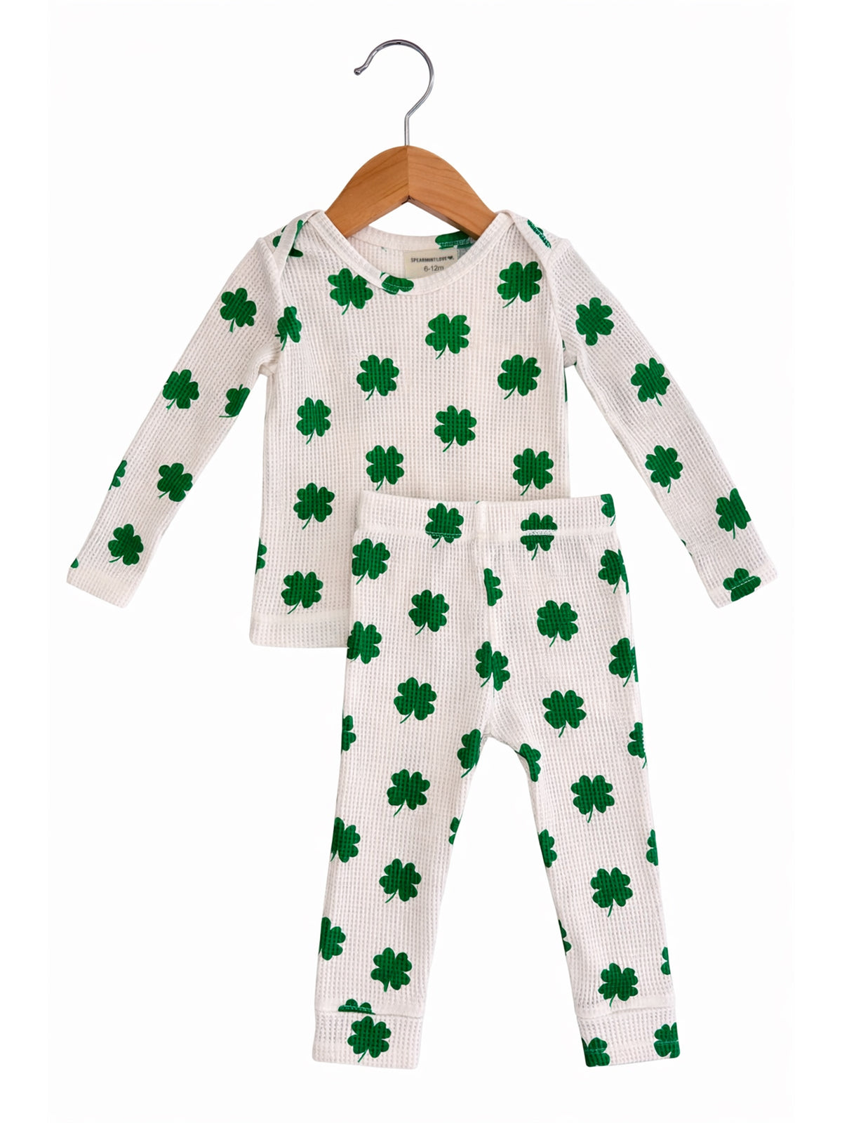 White children's pajama set with green shamrock patterns, hanging on a wooden hanger.