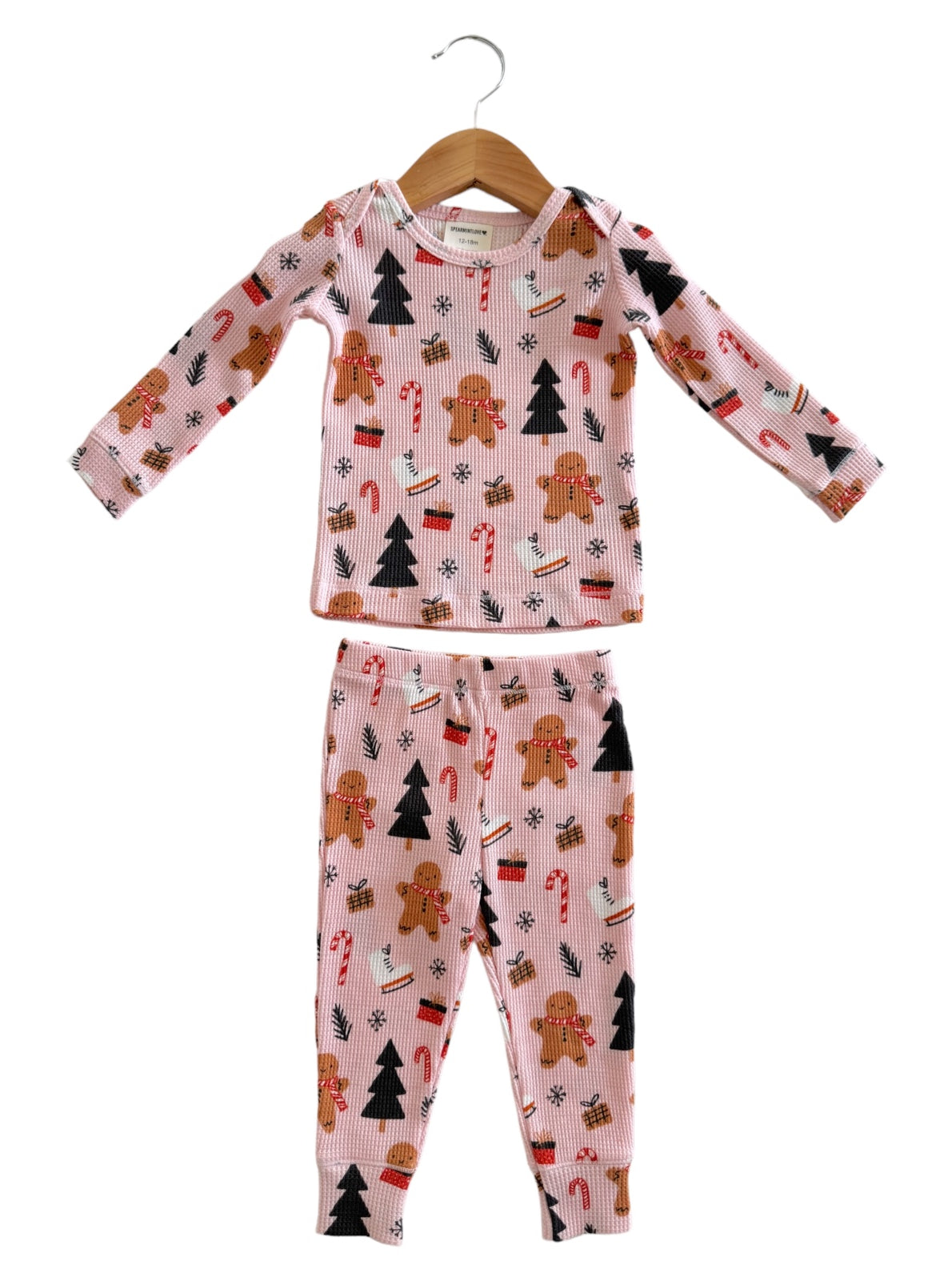 Holiday-themed children's pajamas with gingerbread, candy canes, and Christmas trees, on a pink background.