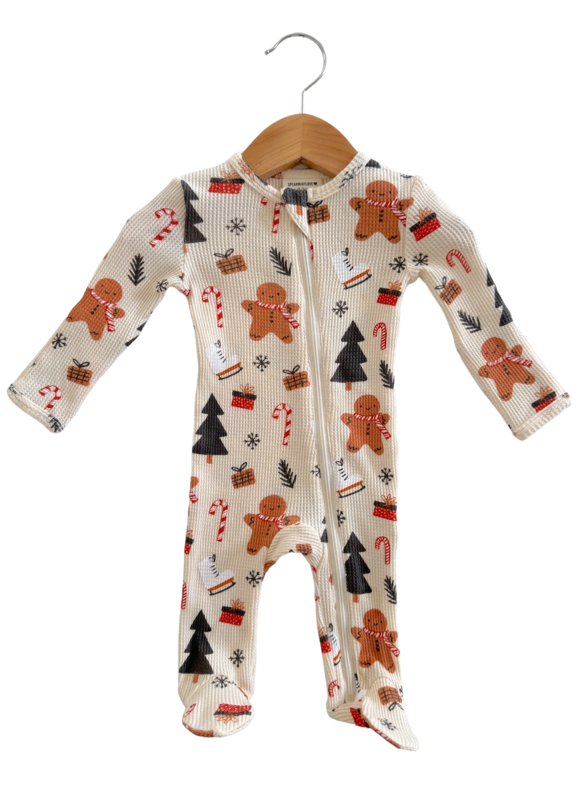 Gingerbread-themed onesie with candy canes and festive patterns, hanging on a wooden hanger.