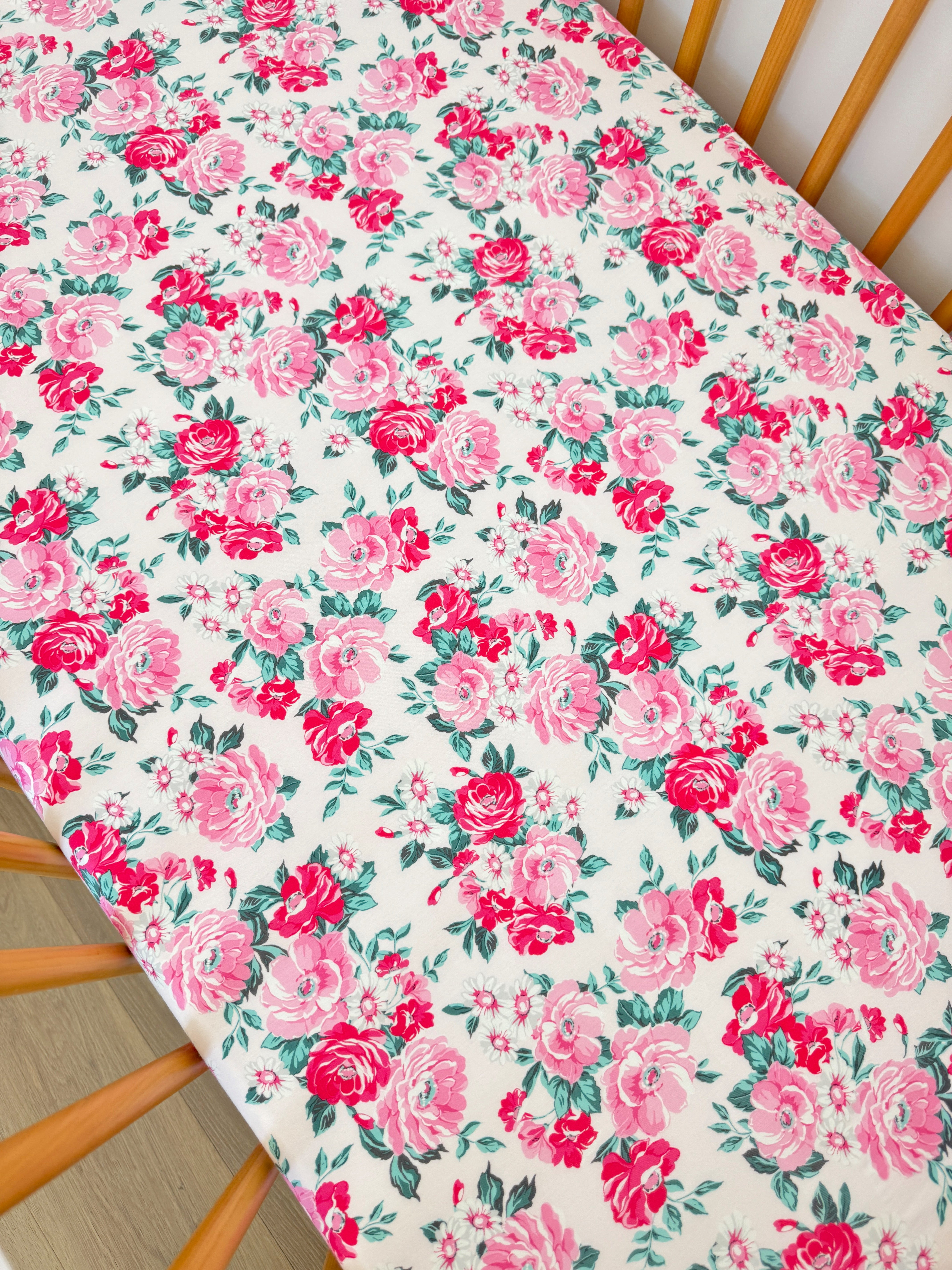 Floral tablecloth with pink roses and green leaves on a light background, draped over a wooden chair.