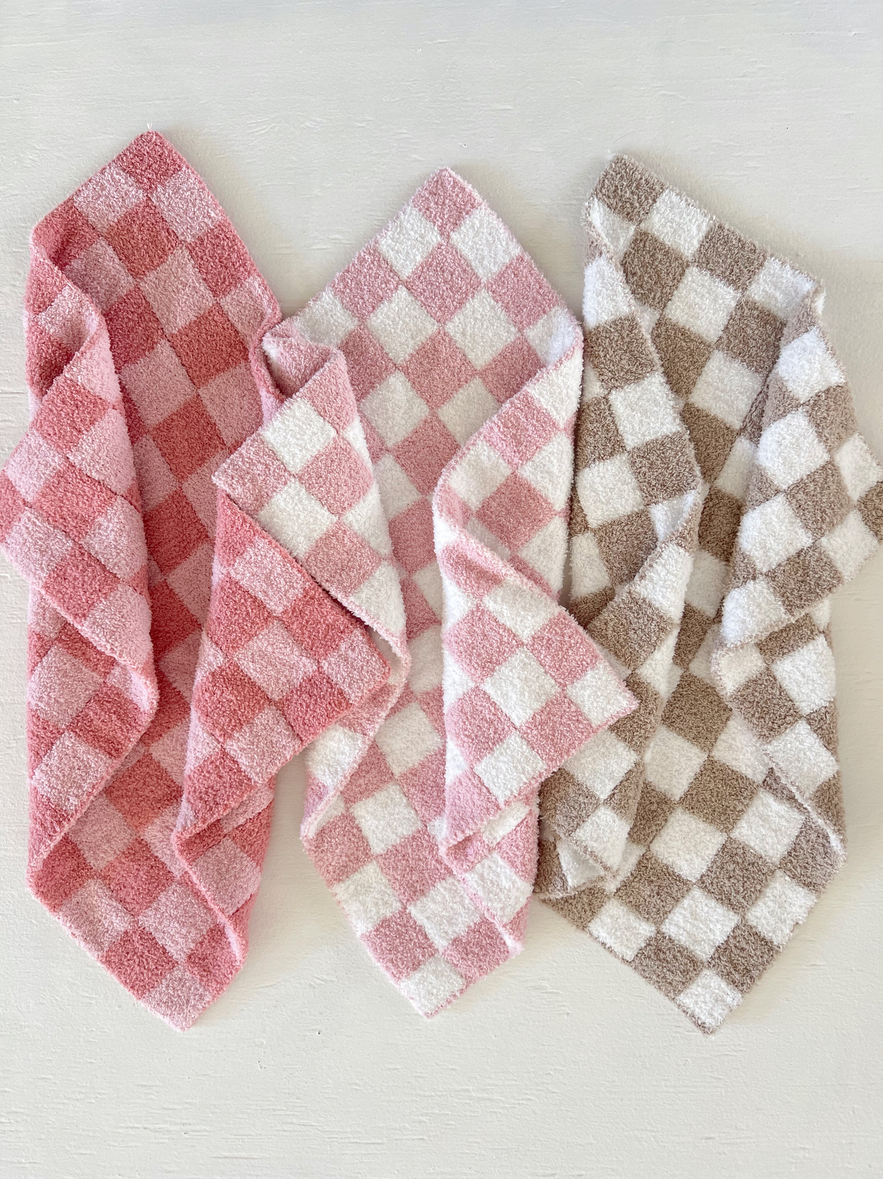 Three folded checkered towels in pink, white, and brown on a light background.