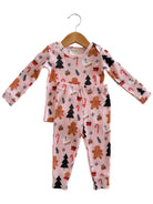 Pink pajama set featuring gingerbread, candy canes, and Christmas trees, hanging on a wooden hanger.