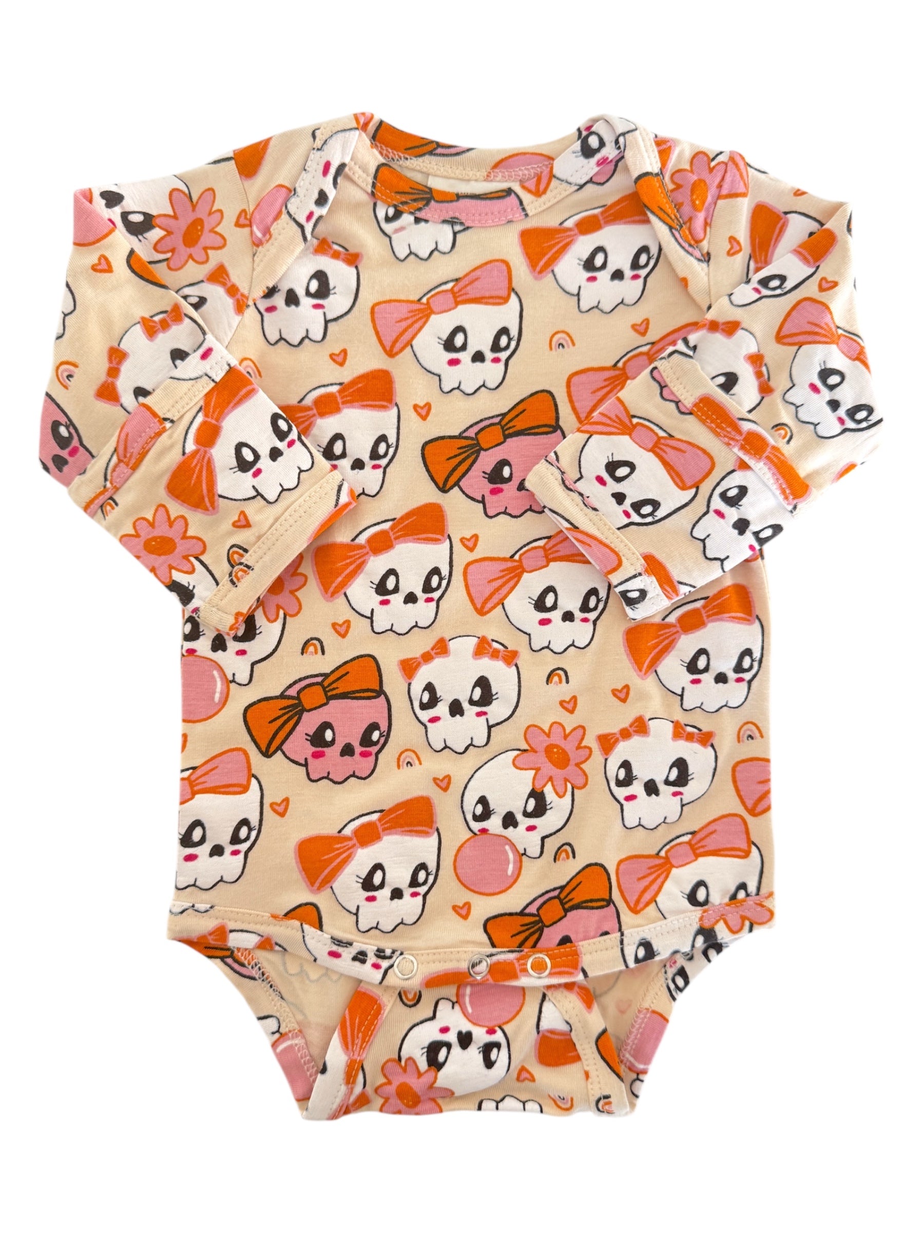 Long-sleeve baby onesie with a playful skull and bow pattern in pastel colors against a cream background.